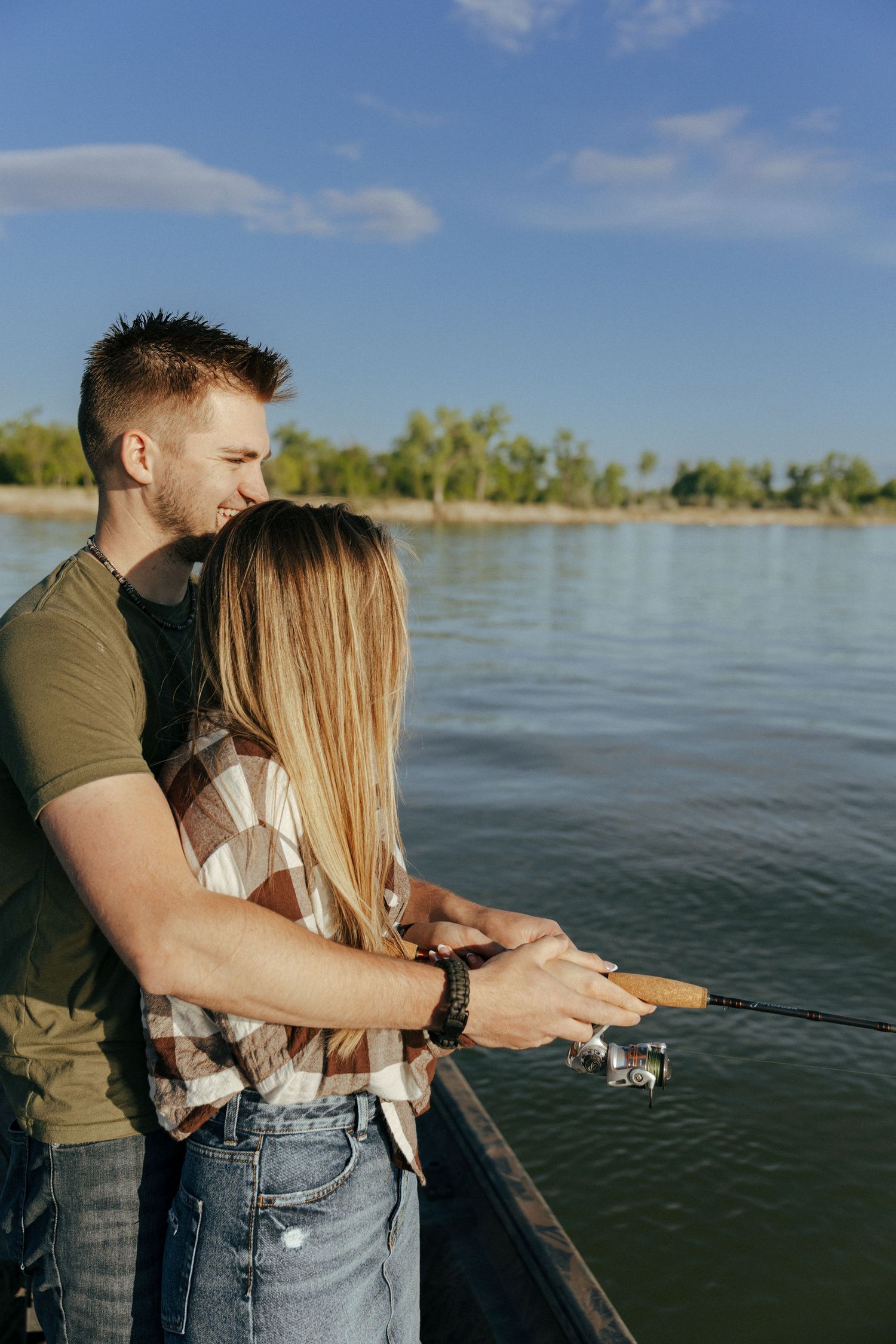 Couple enjoying a fishing moment together by a serene lake on a sunny day.