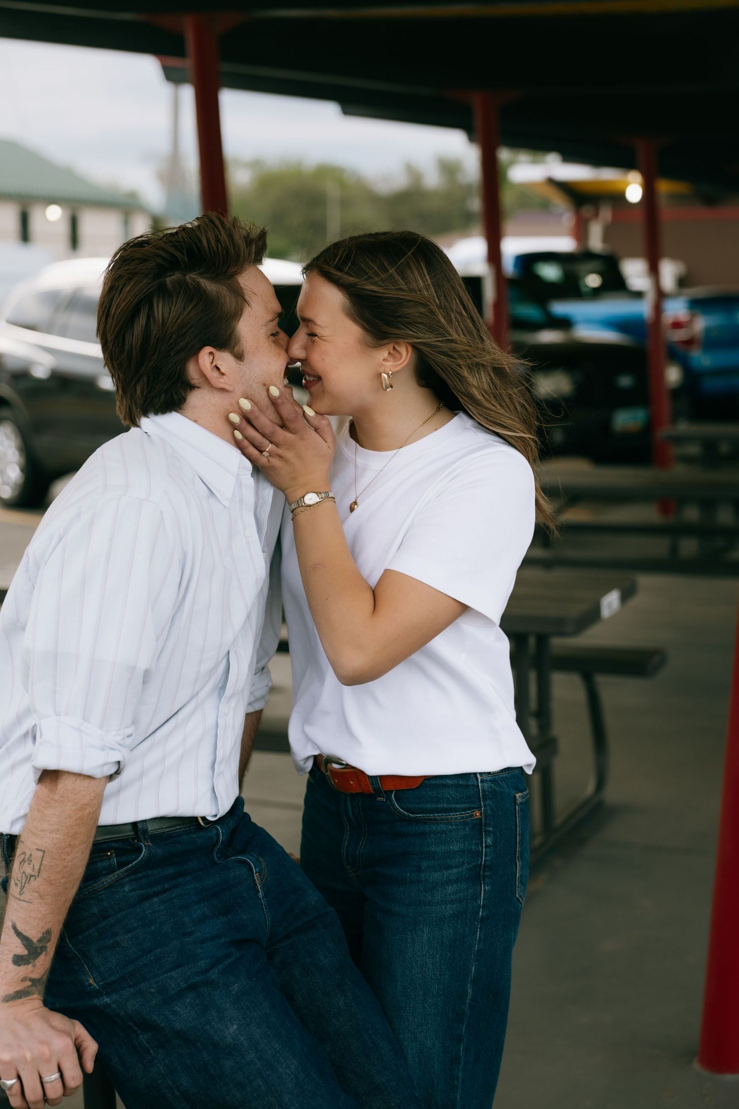A couple shares a romantic moment, smiling and touching foreheads outside a diner parking lot.