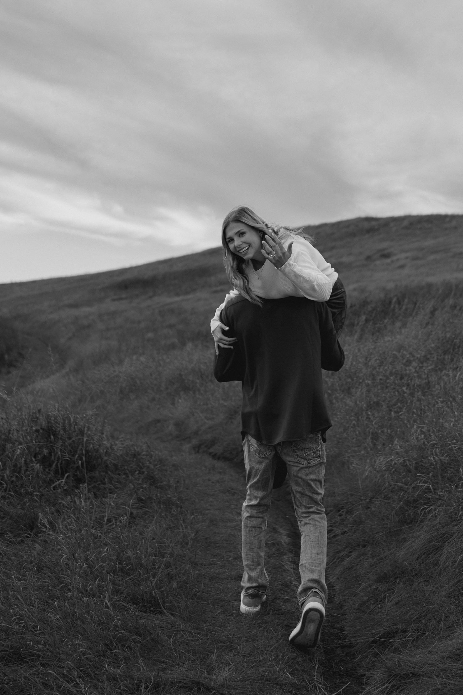 Someone poses casually on a winding dirt path through rolling hills.