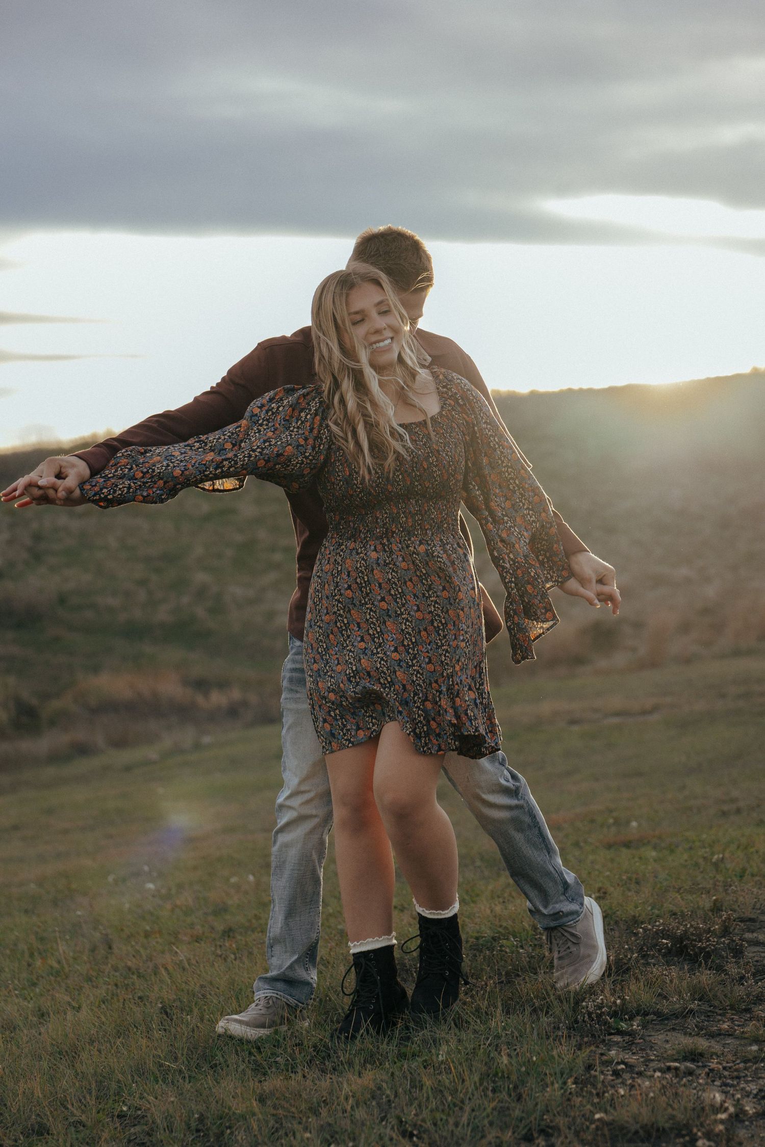 Two people dance together on a hillside at sunset near a lake.