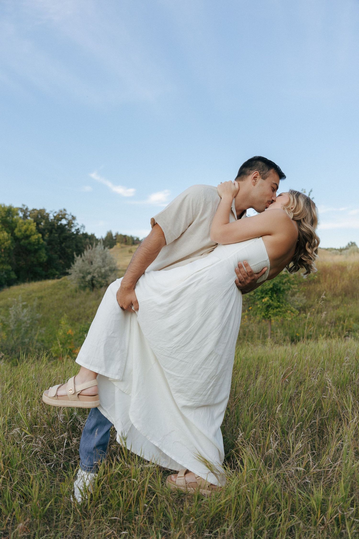 A romantic dip kiss captured against a blue sky and natural landscape.