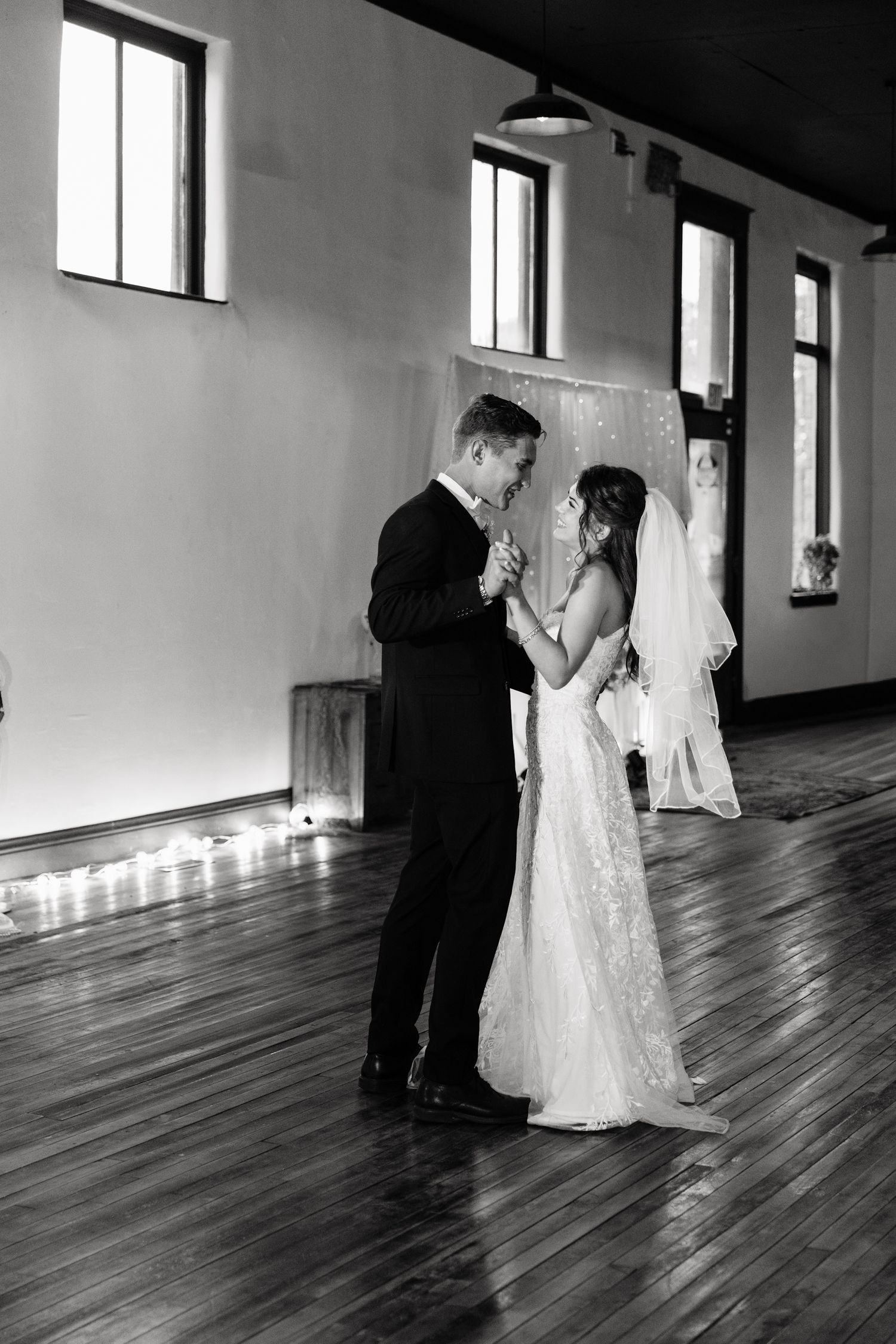 Black and white photo of bride and groom sharing their first dance in an elegant indoor venue with wooden floors.