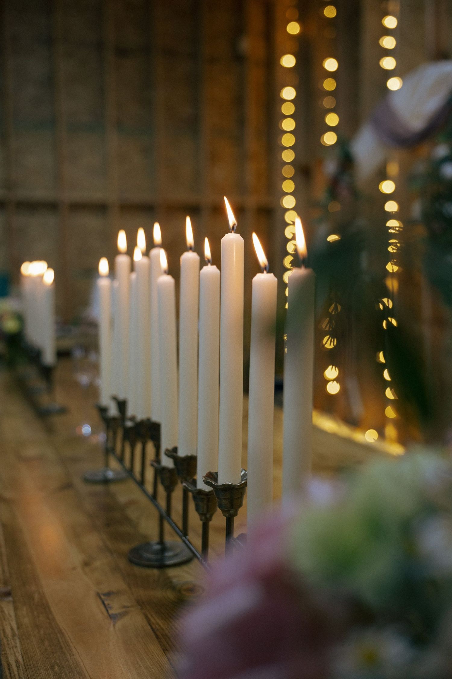 Row of elegant white candles glowing on a rustic wooden surface with bokeh lights in the background.