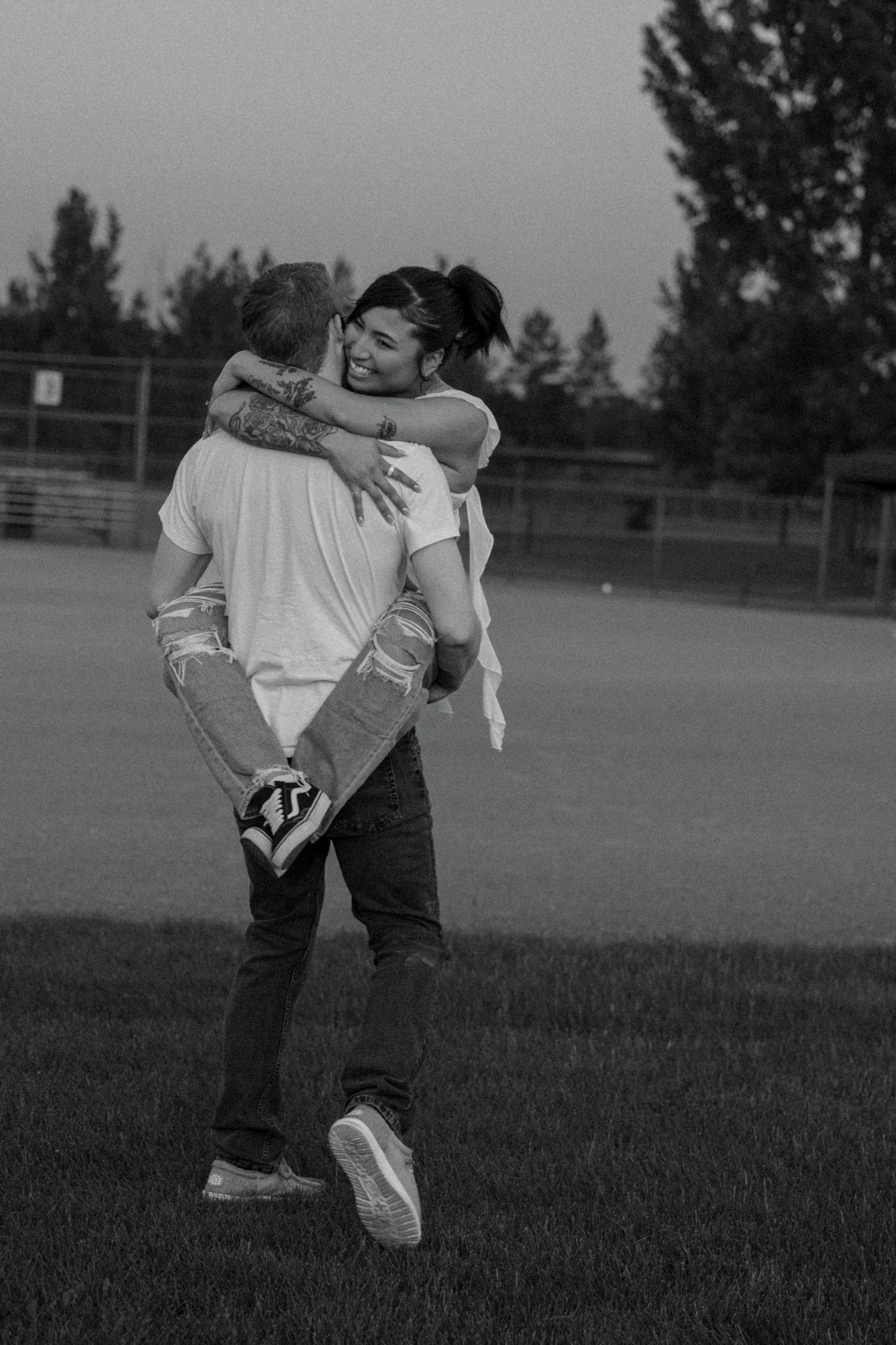 Black and white photo of a couple dancing playfully in a grassy field.