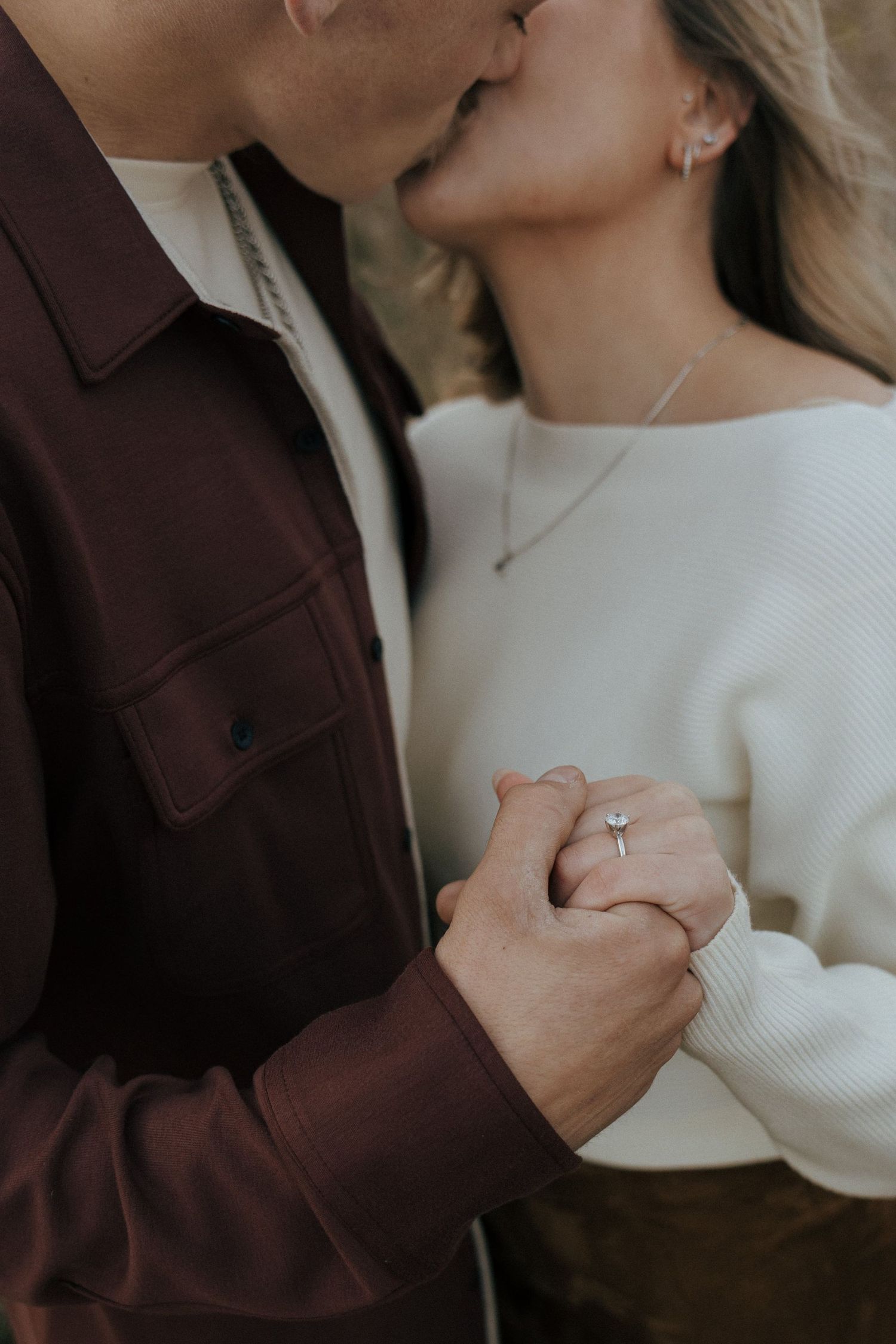 couple kissing as man holds engagement ring up