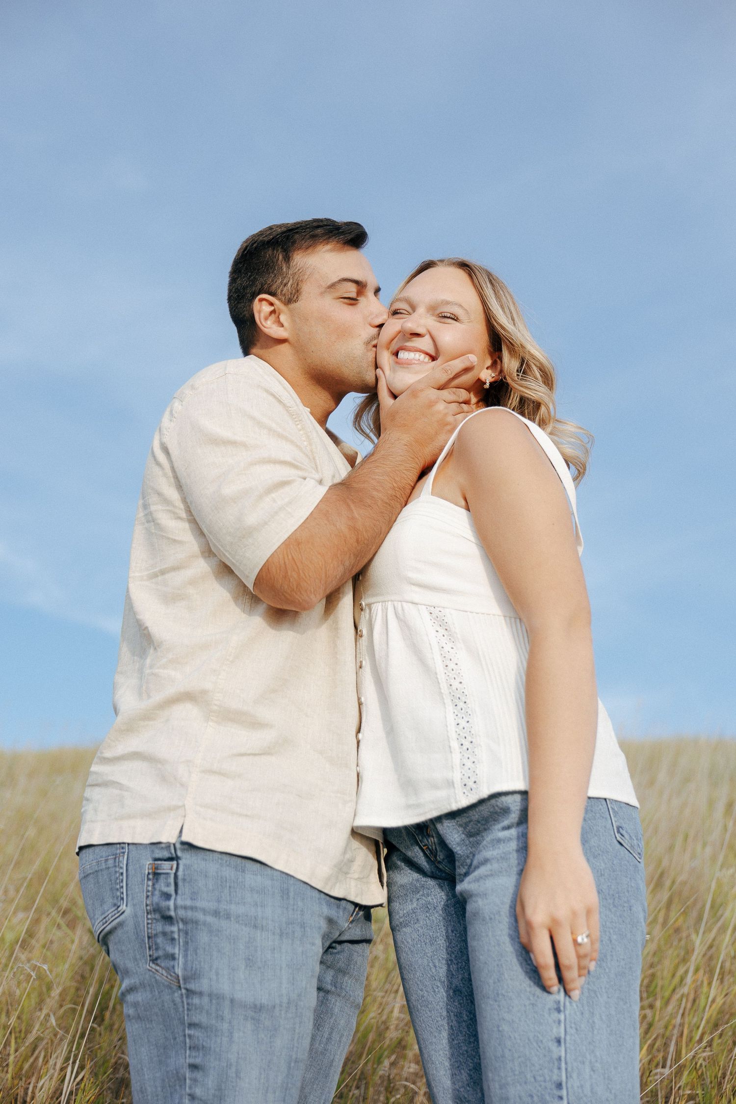 Romantic couple in casual attire sharing an intimate moment in a grassy field.