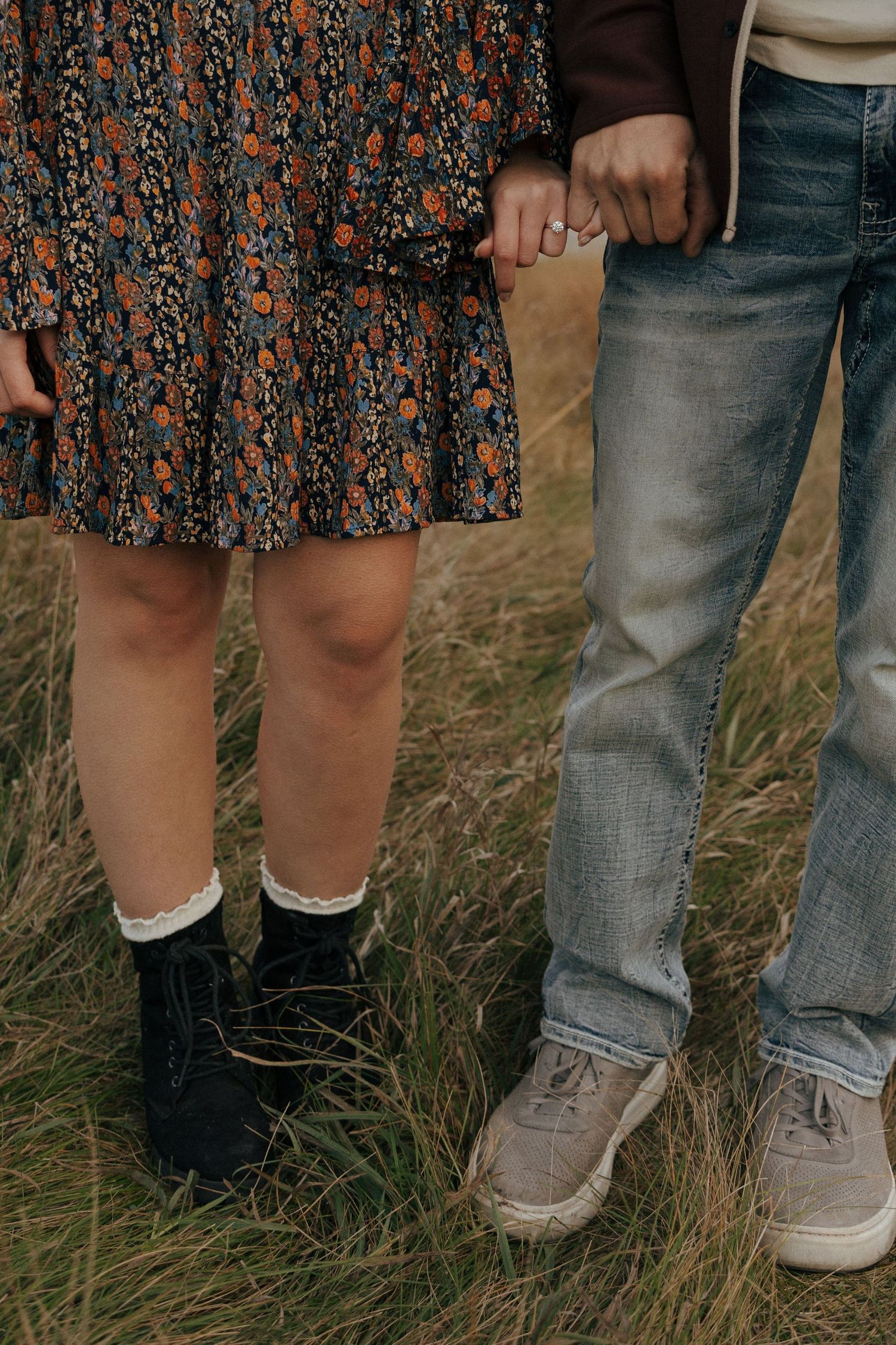Candid lower body shot showing floral dress and jeans in a grassy field.