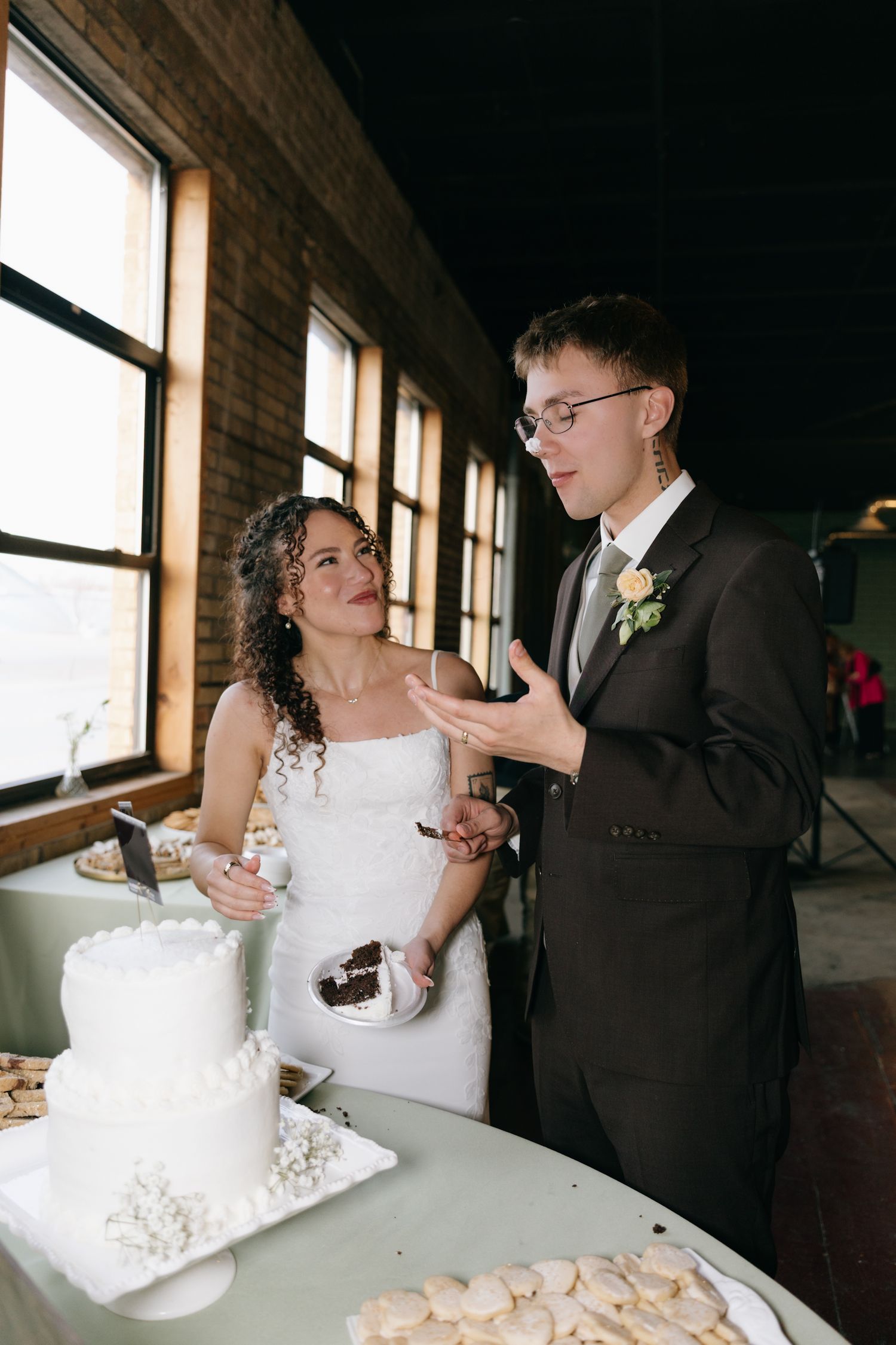 Bride and groom cutting their white wedding cake at a rustic venue, sharing a joyful moment together.