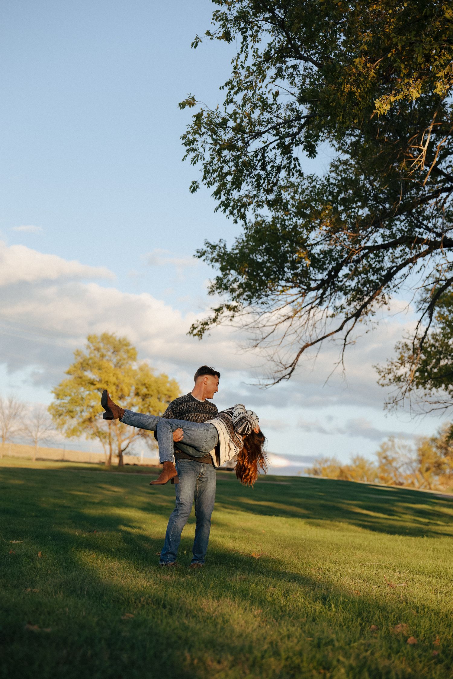 man spinning girl in arms as they play as a couple in a grassy field at sunset
