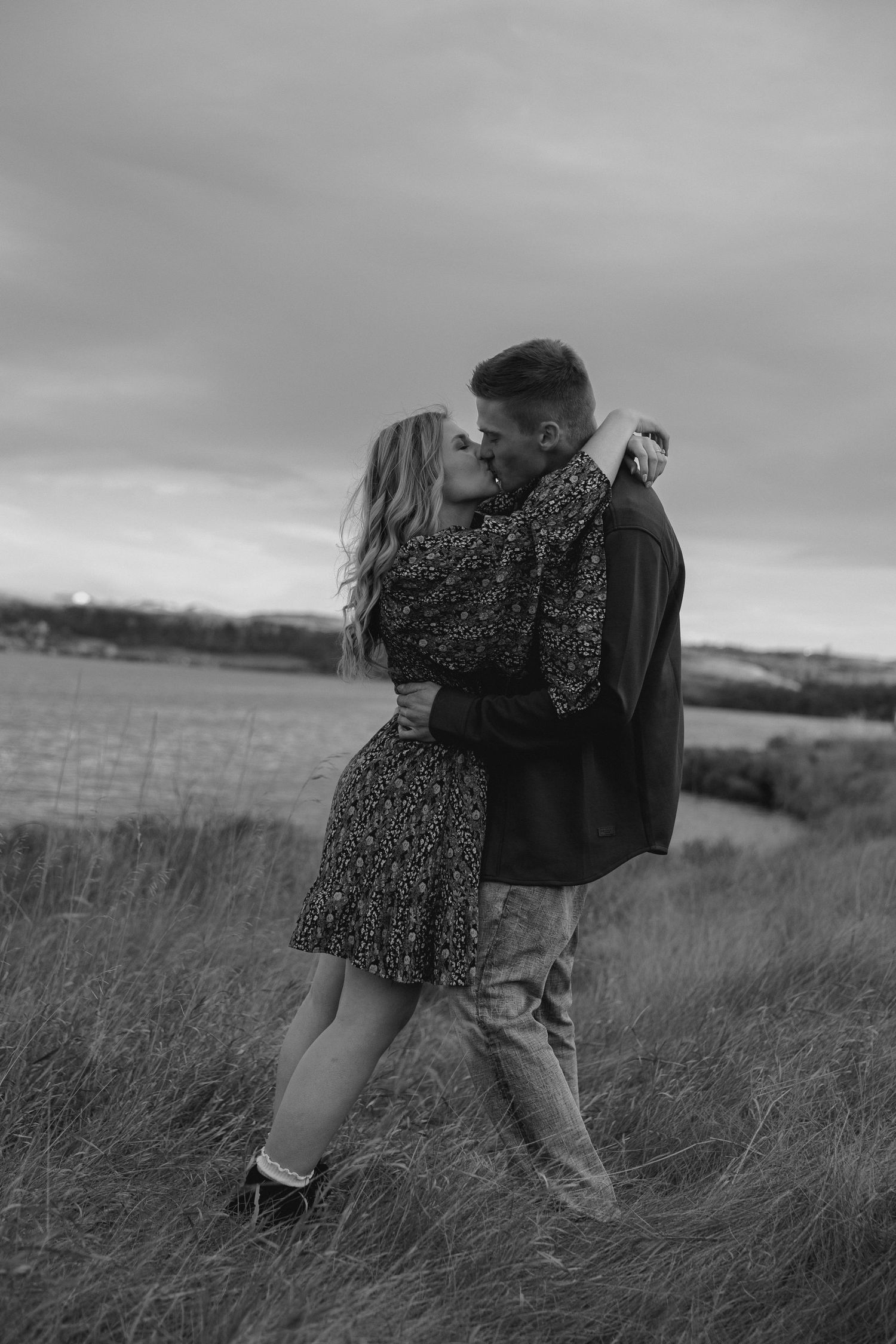 Black and white photo of couple embracing in windswept field.