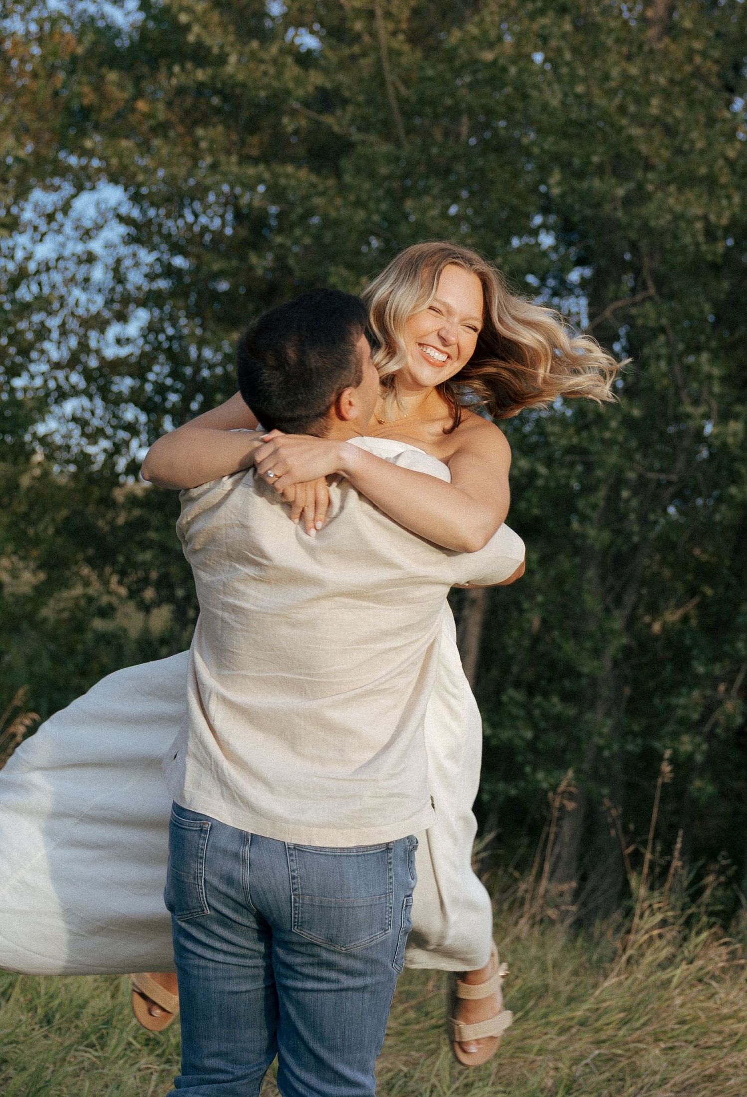 Two people share a joyful embrace in a natural outdoor setting with trees in the background.