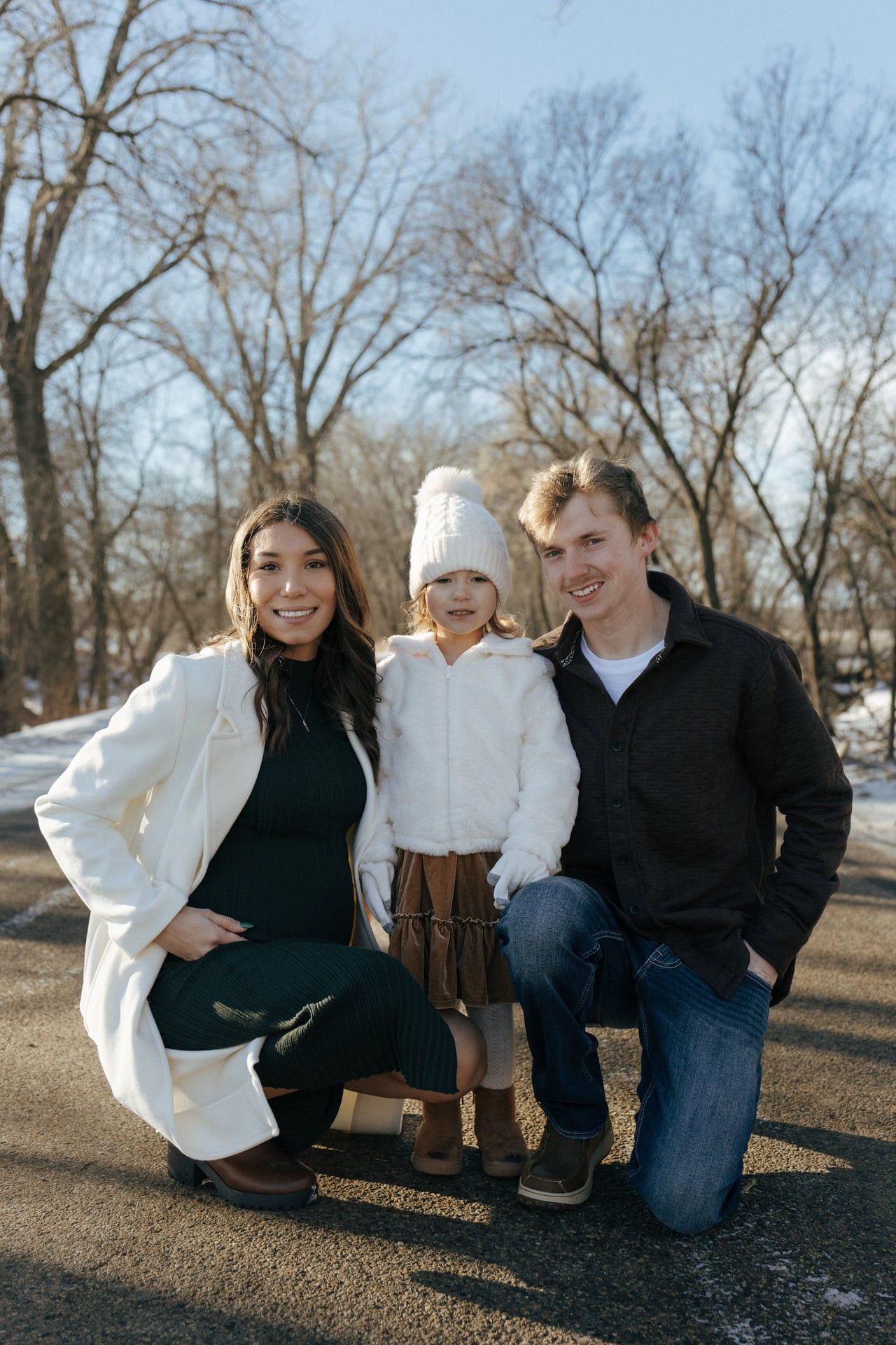 photos of mom and dad crouching down next to daughter in snowy trees in Bismarck