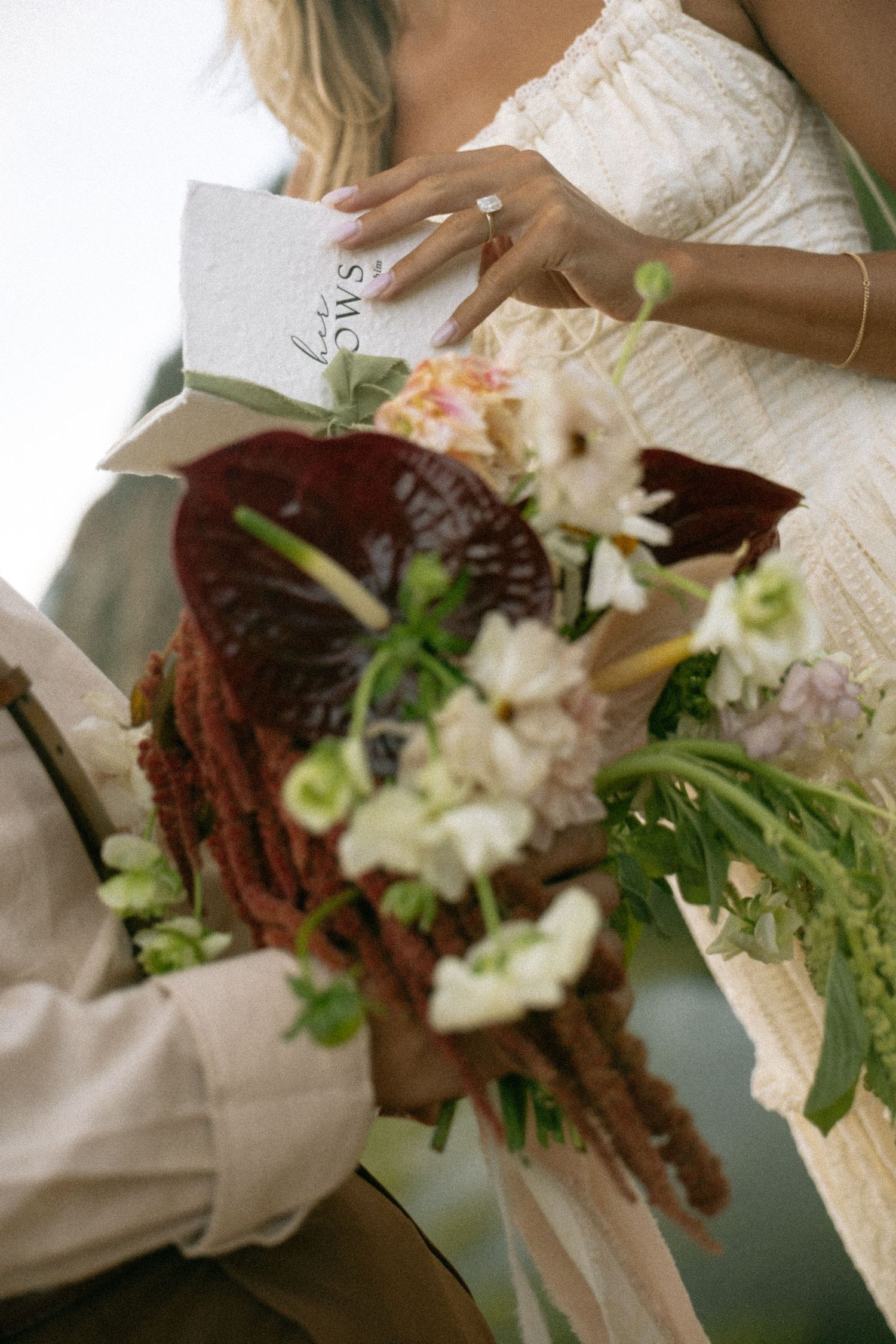 Bride holding wedding vows booklet and bouquet with dark red anthuriums and white flowers at ceremony.