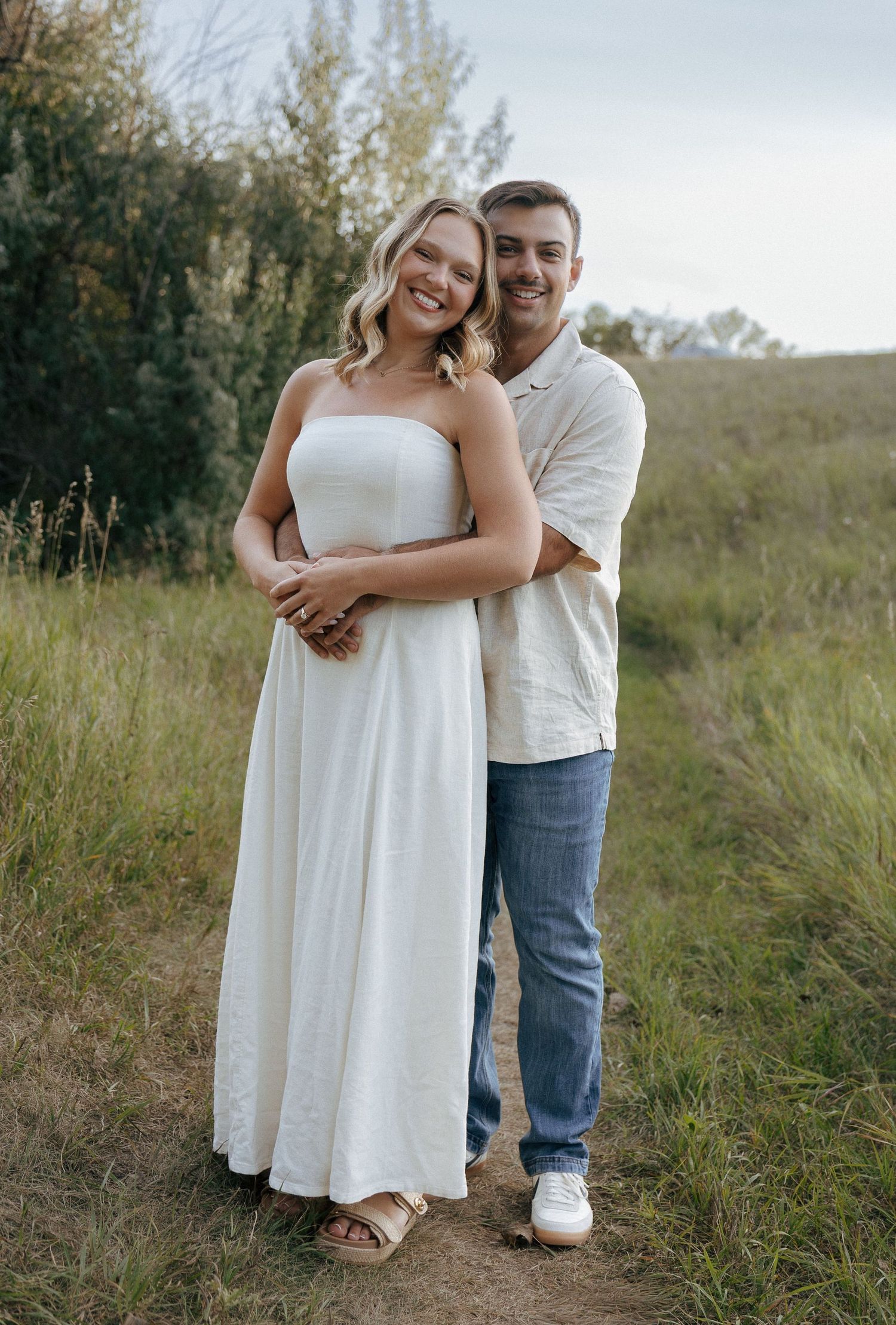 A couple embraces while standing on a nature trail during their engagement photoshoot.