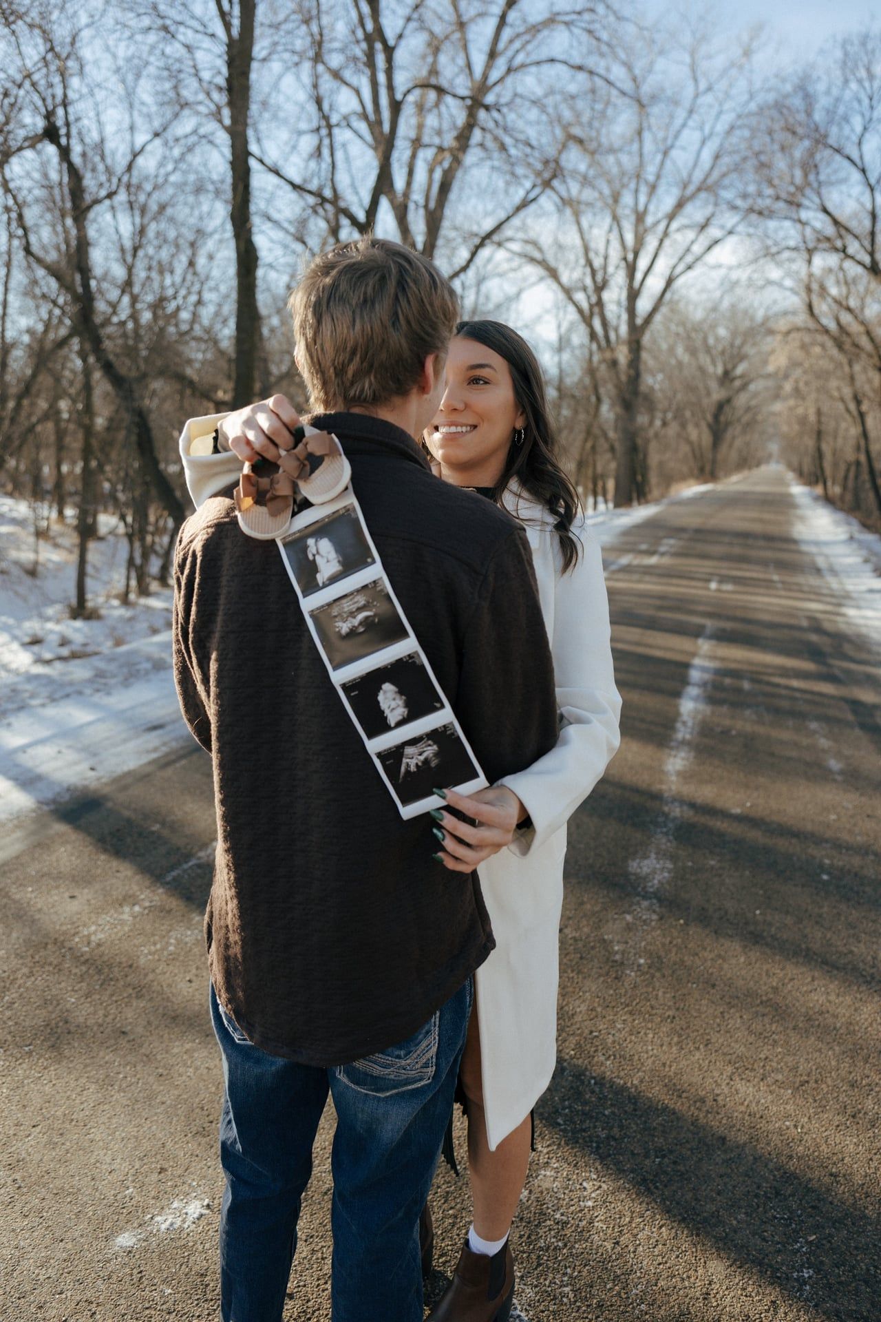 Couple smiling at each other in snowy trees in Bismarck with ultrasound photos