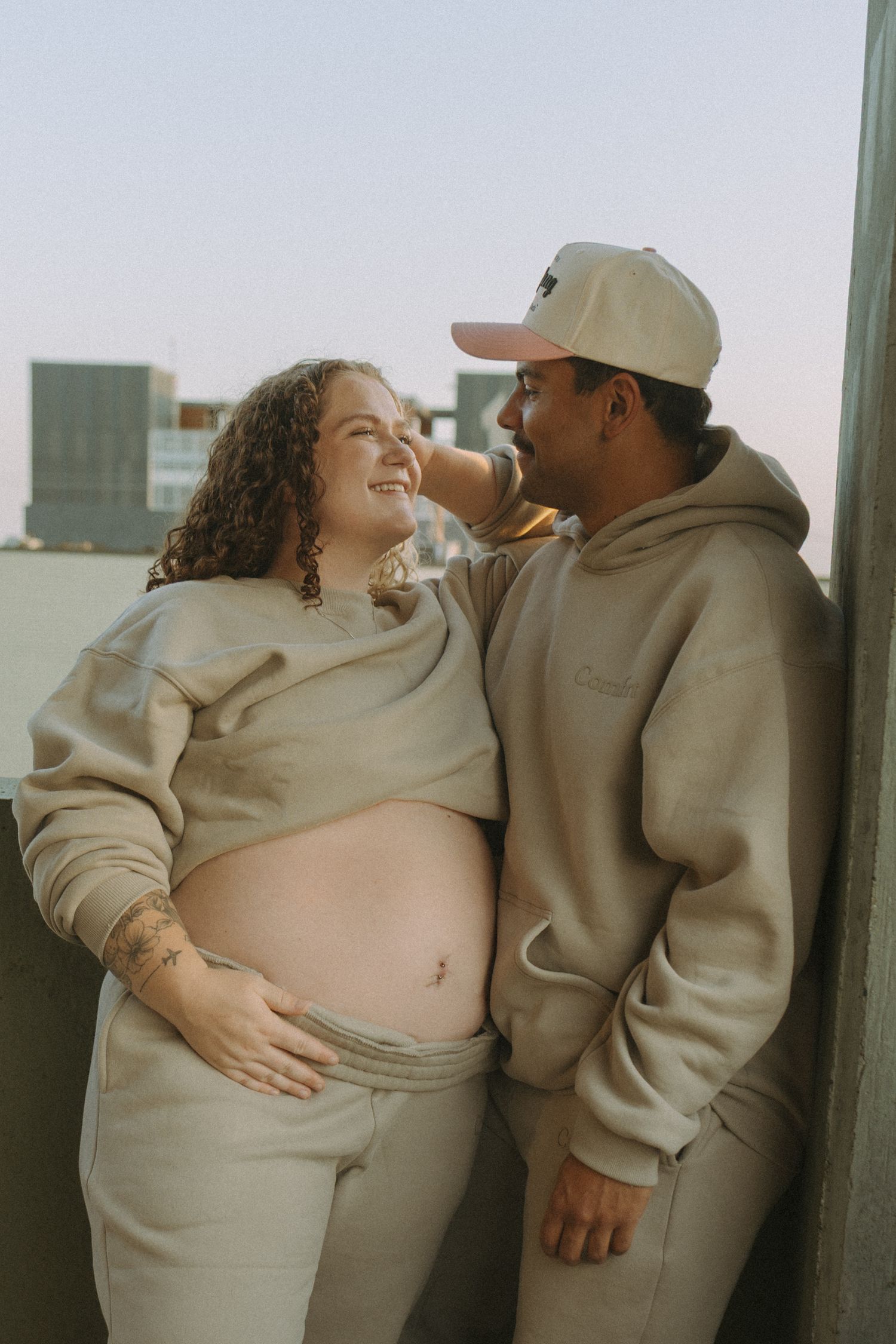 couple smiling looking at each other while holding baby bump for maternity session downtown Bismarck