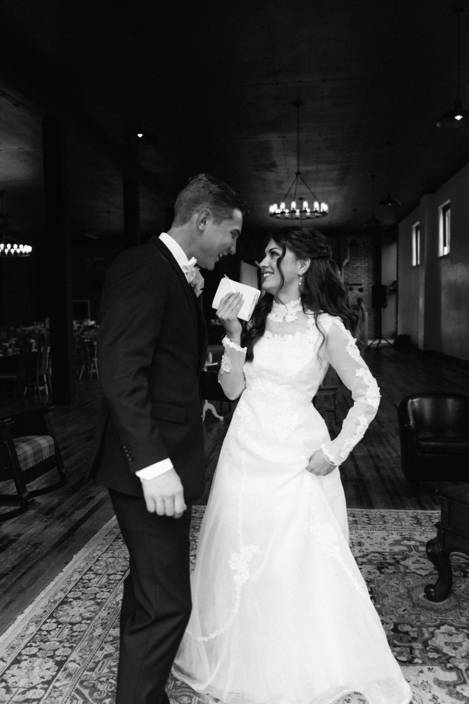 Bride and groom share a joyful moment during their first dance in a rustic indoor wedding venue.
