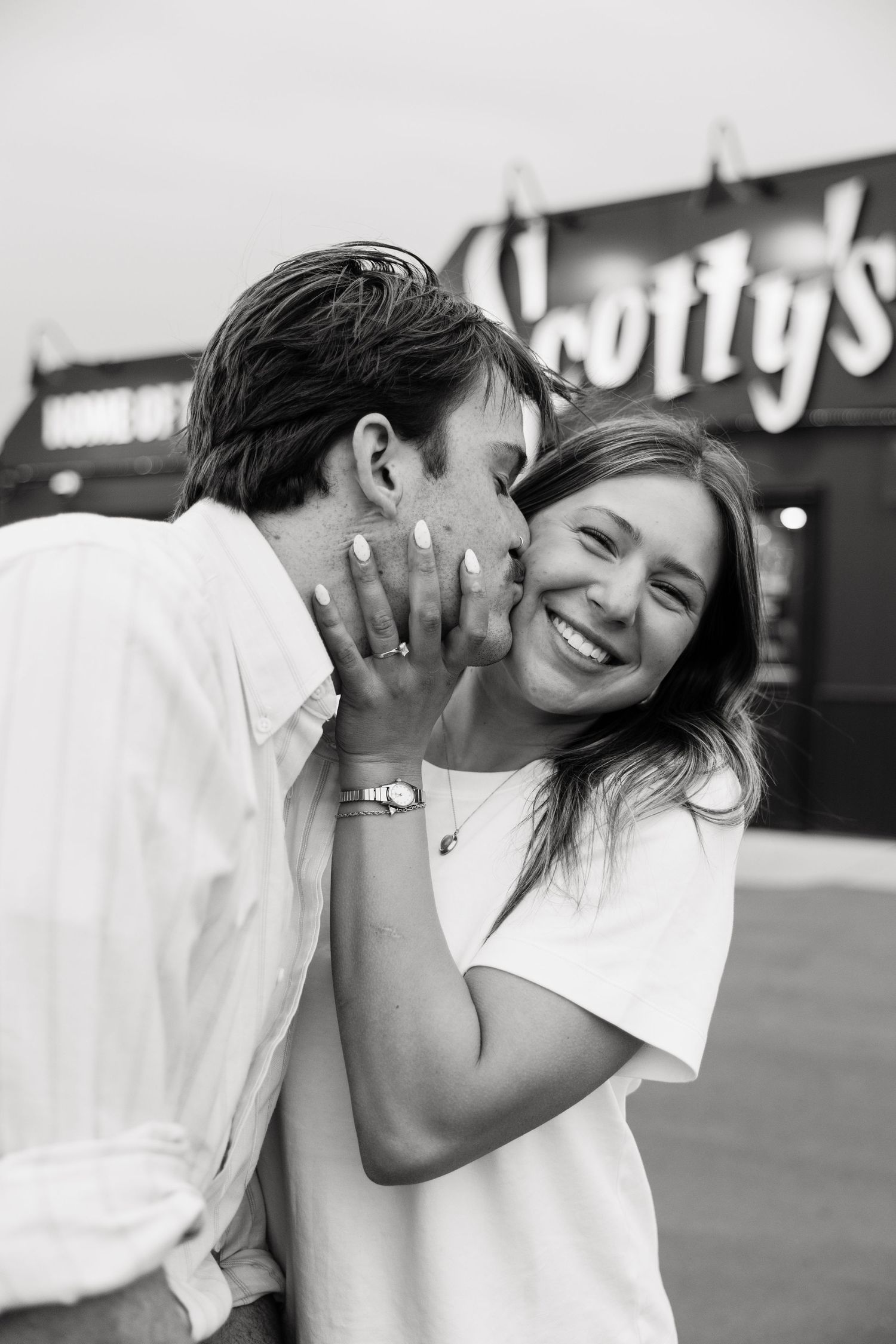 Black and white photo of man whispering to laughing woman outside Scotty's diner.