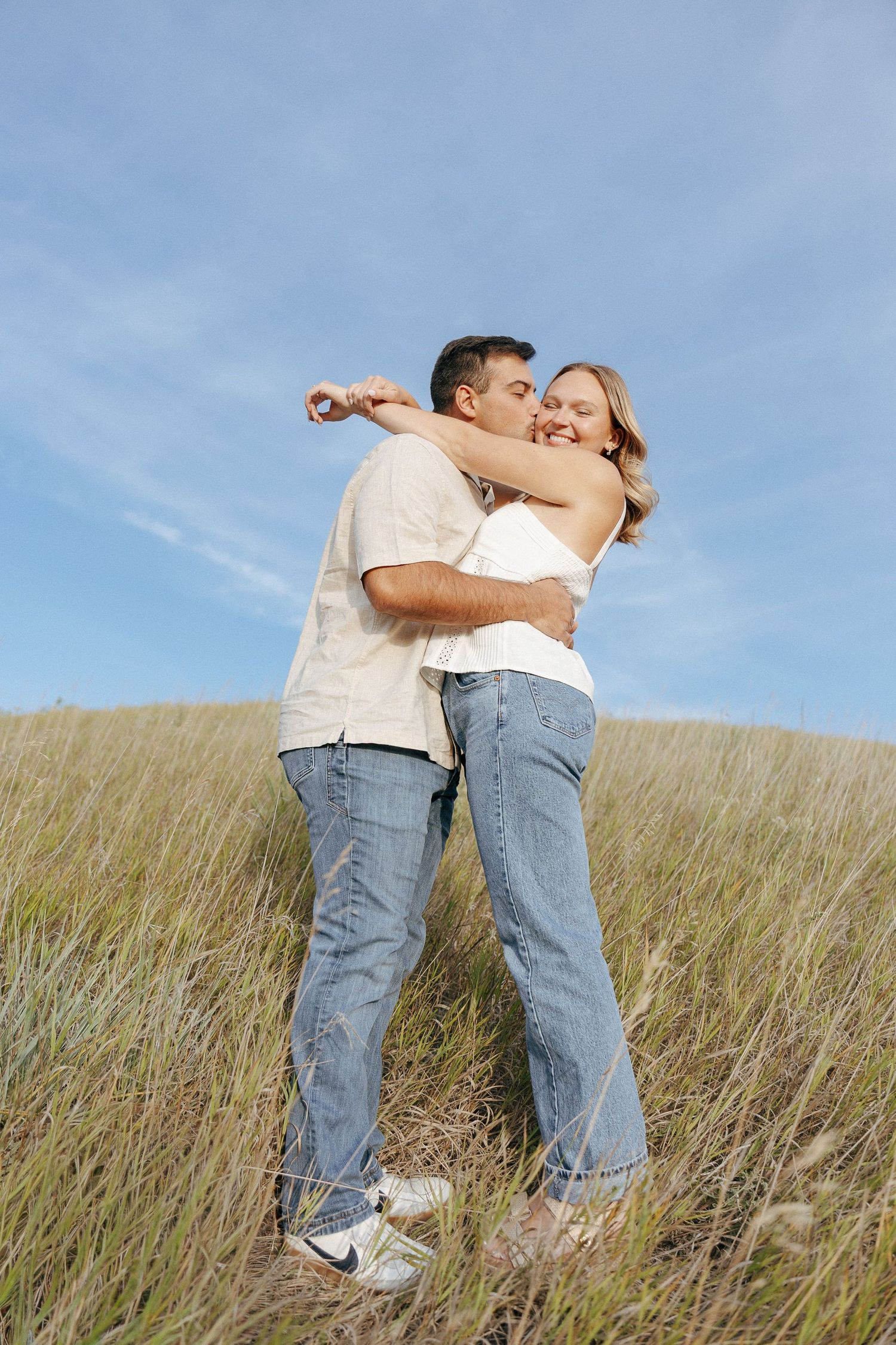 Two people sharing a romantic moment while standing in tall grass under blue skies.
