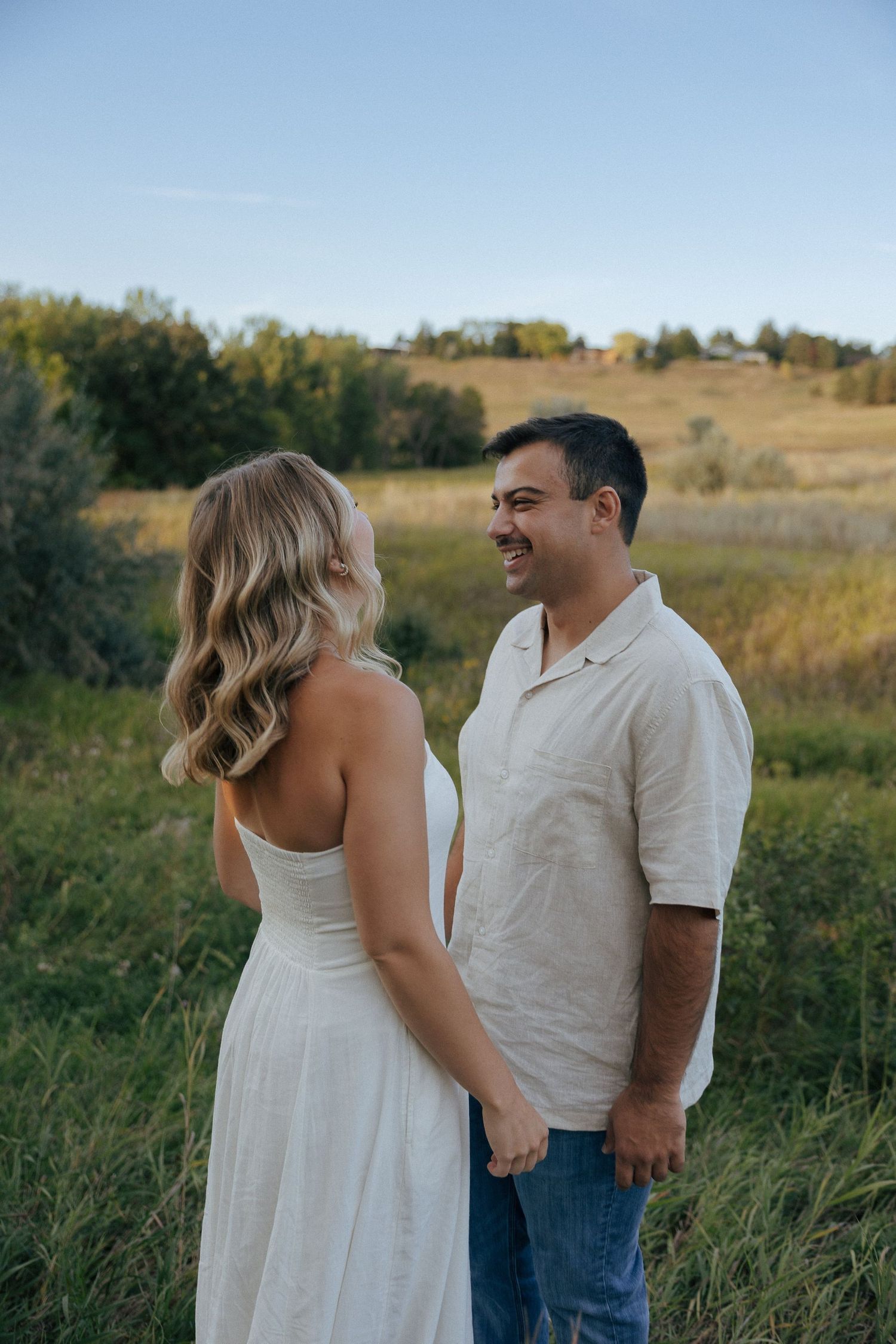 A joyful couple sharing laughter together in a sunlit field with rolling hills.
