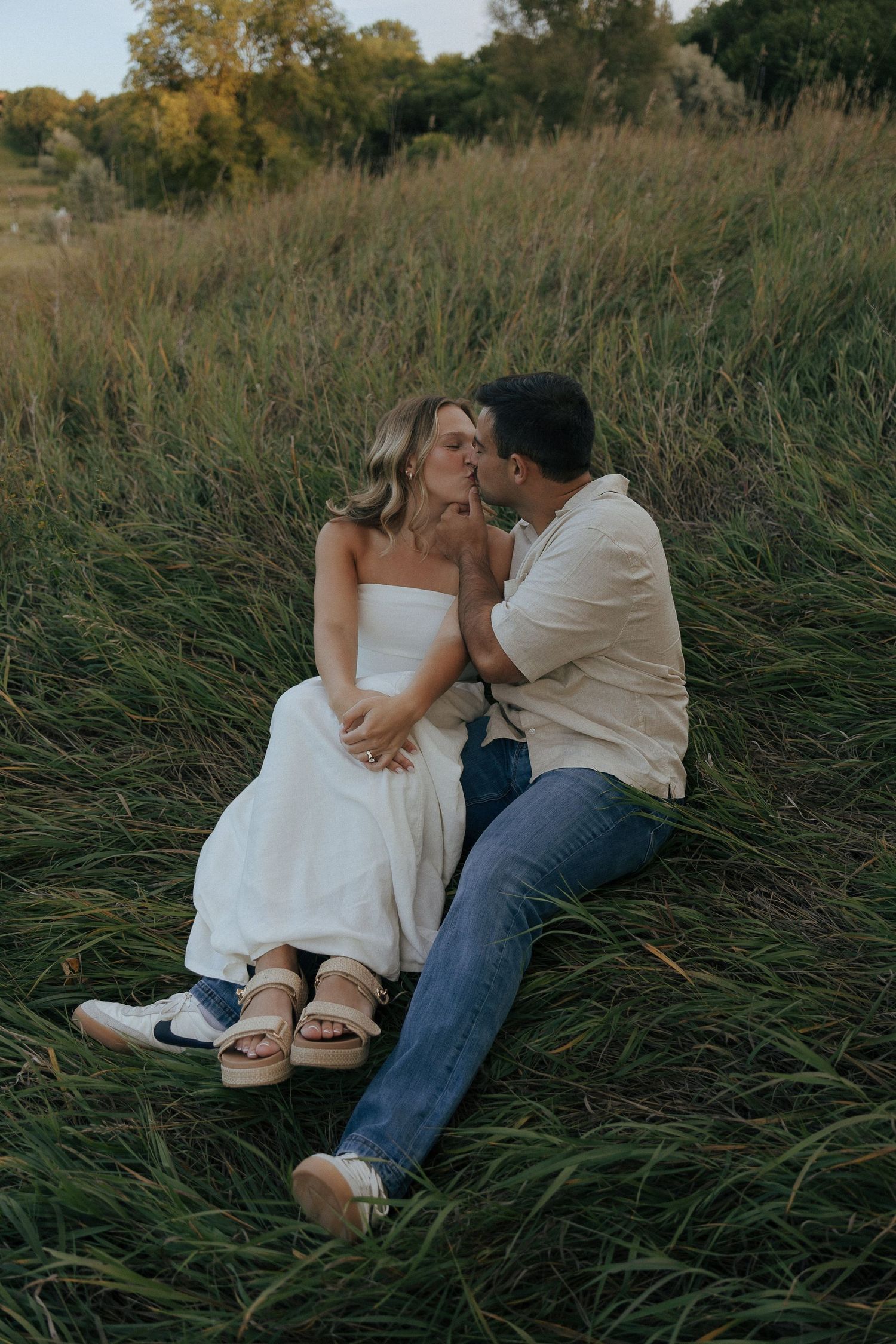 A couple relaxes together in a grassy meadow during their engagement photo session.