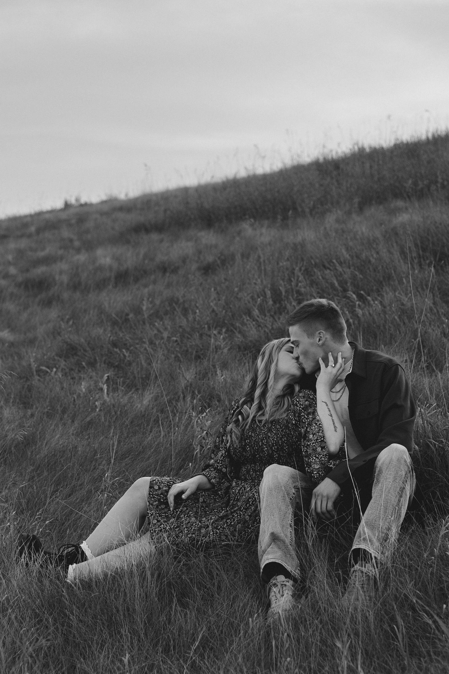 Black and white photo of couple lying in meadow grass during intimate photoshoot.