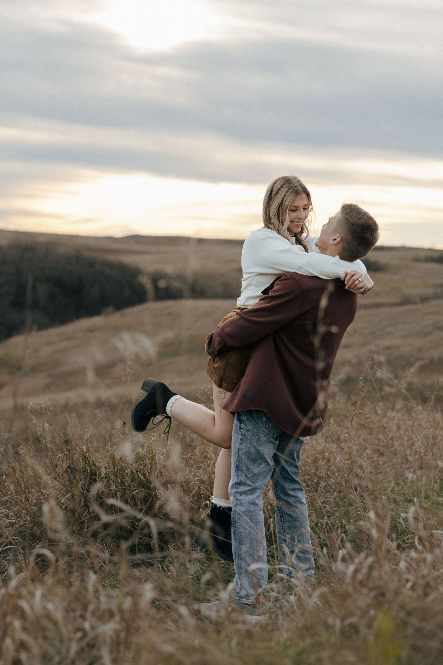 Romantic couple embracing and spinning in a field during sunset.