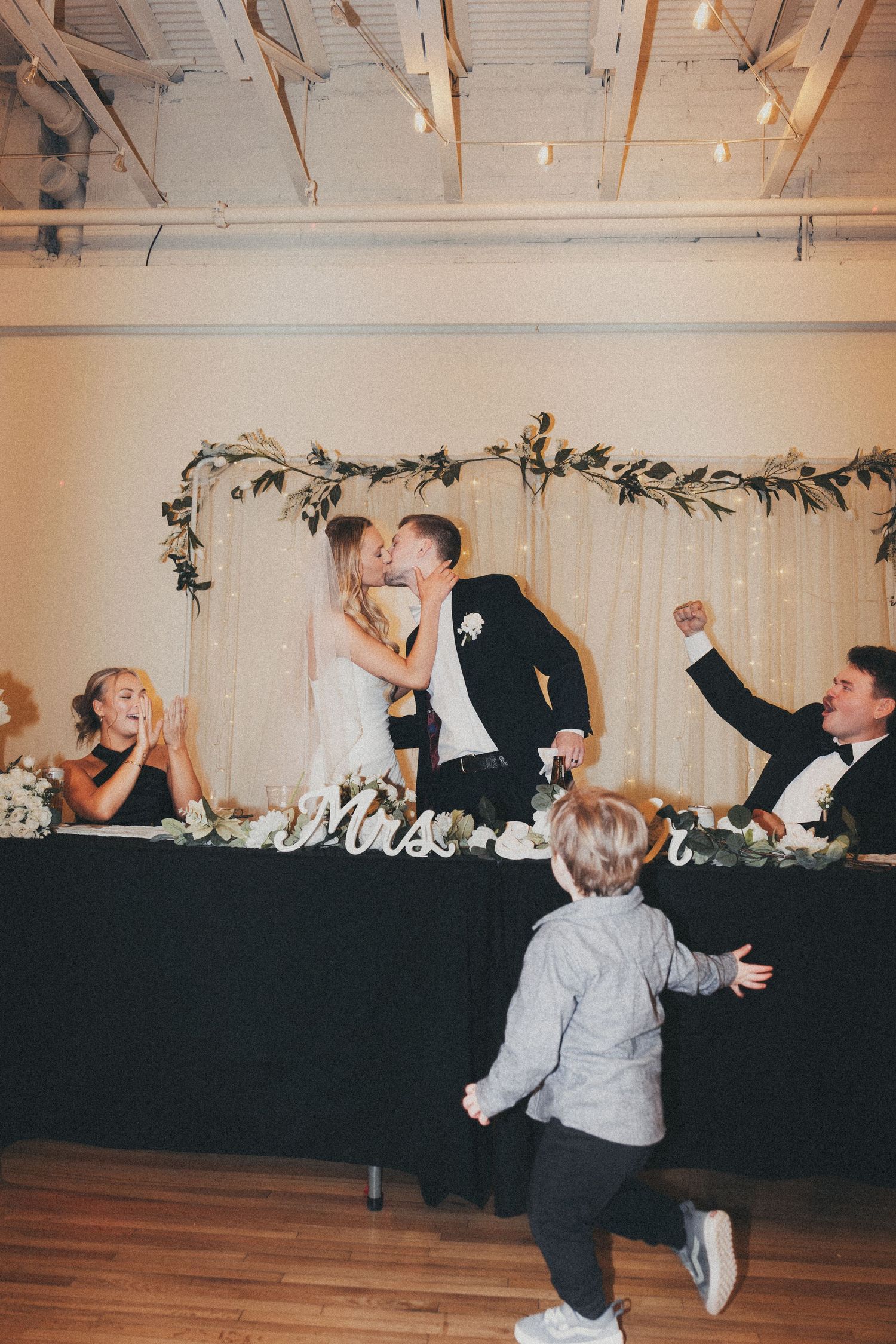 Wedding reception scene with guests dancing and celebrating in a decorated indoor venue.