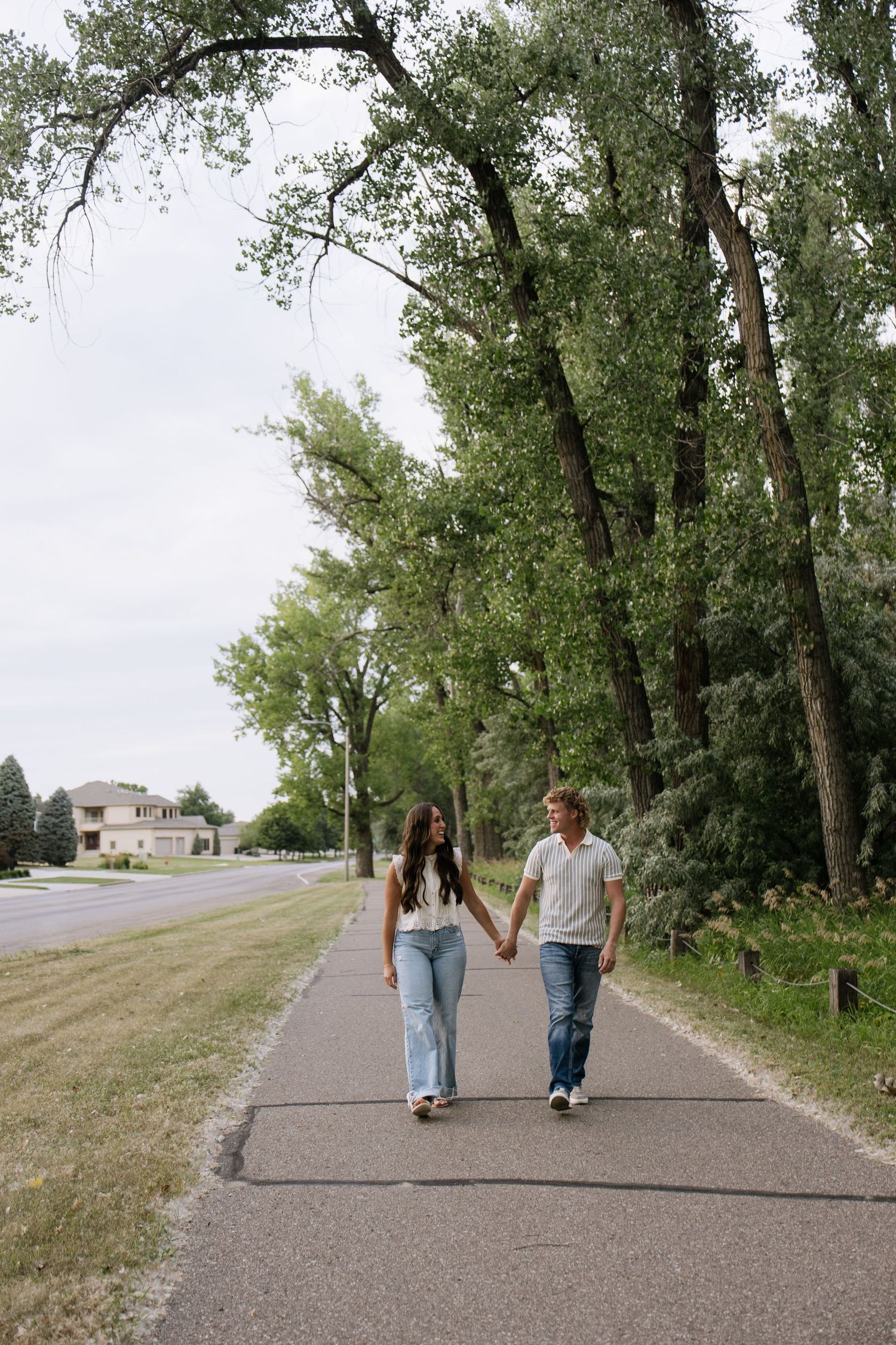 Couple holding hands walking on a tree-lined path in a suburban neighborhood on a cloudy day.