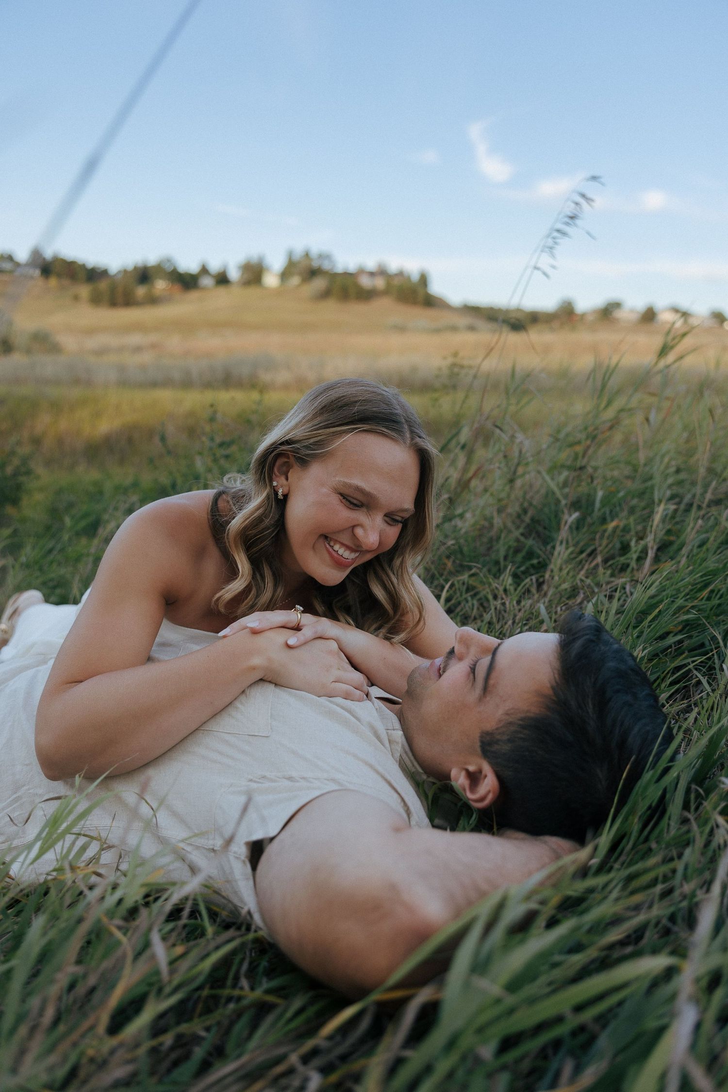 A couple lying in tall grass sharing an intimate moment during golden hour.