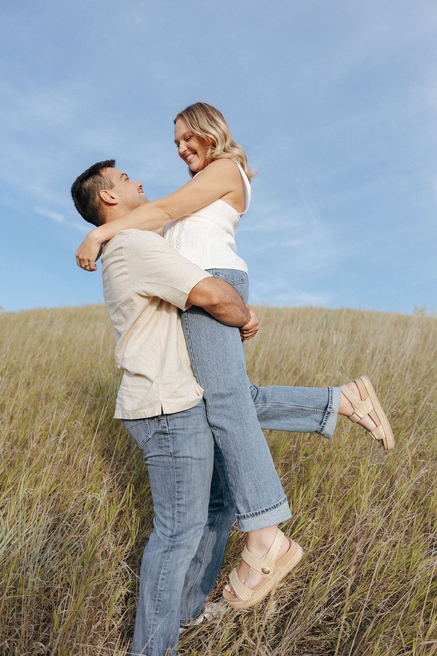 A playful couple embraces and spins around in a grassy field on a sunny afternoon.