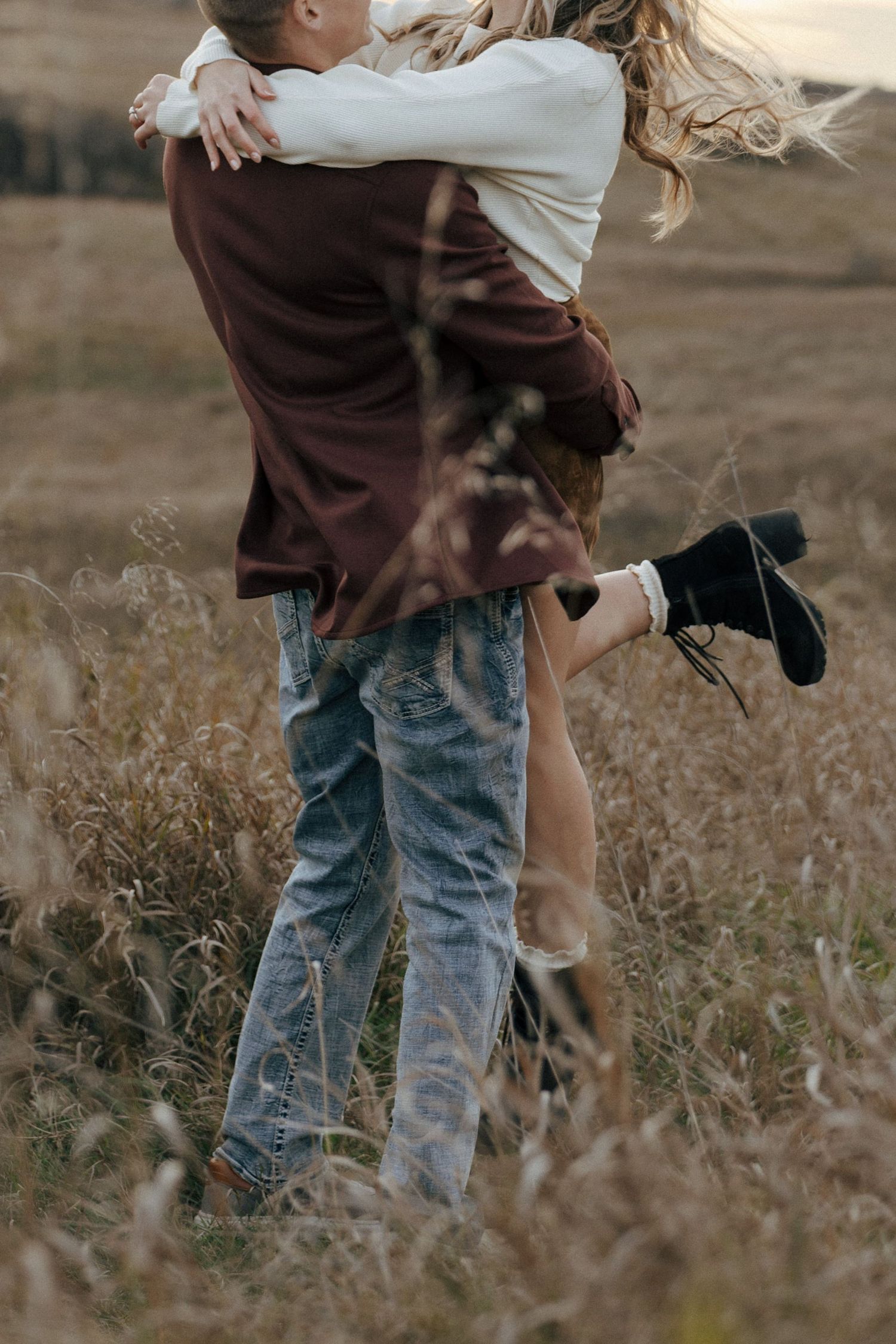 Couple in casual wear embracing in tall grass during golden hour.