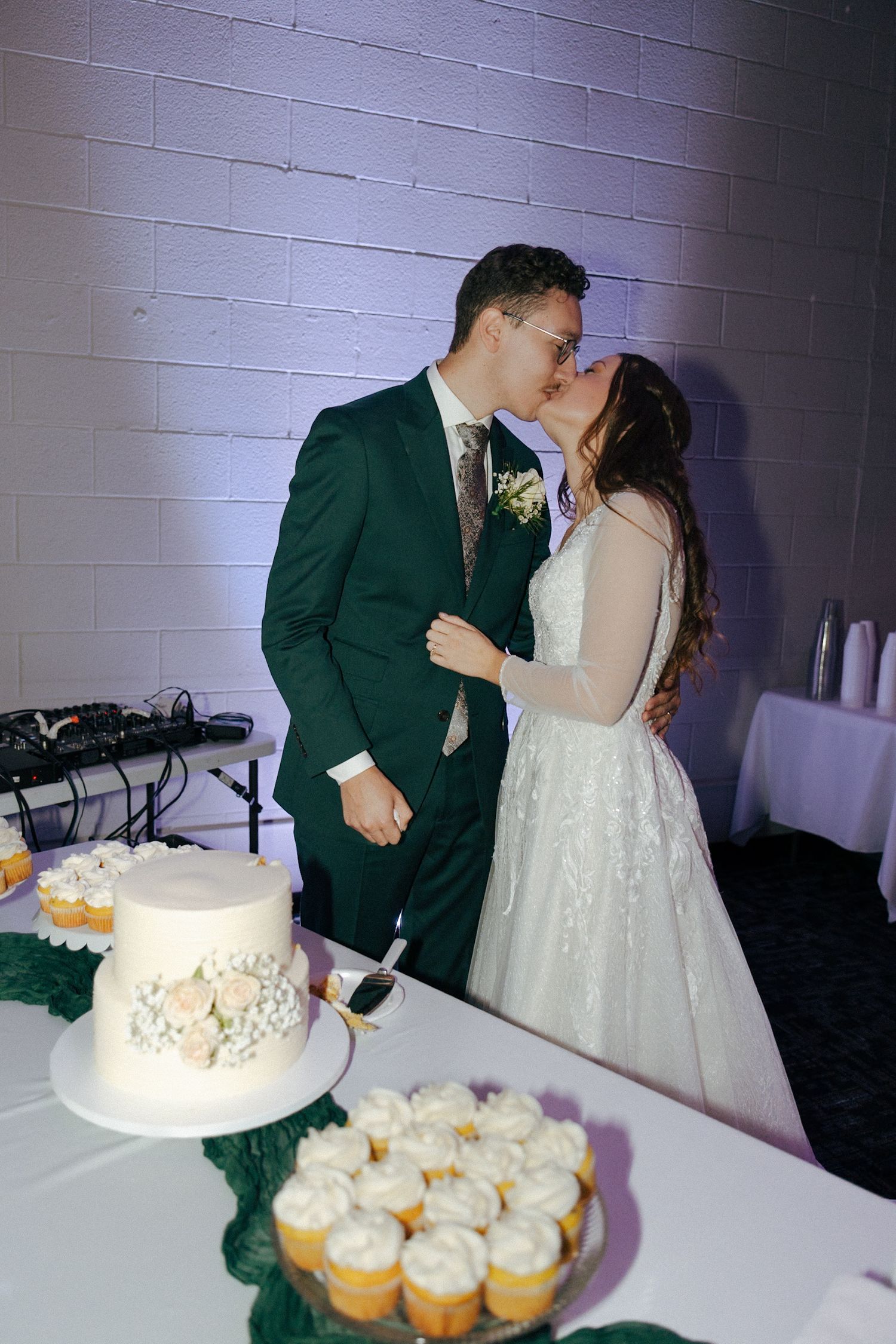 A wedding couple shares a kiss while cutting their cake at the reception.
