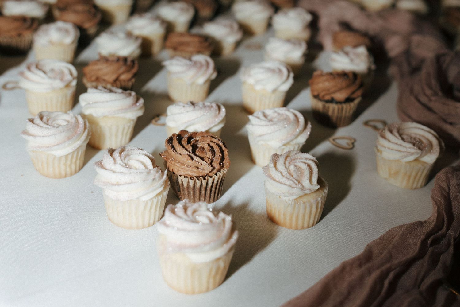 White frosted wedding cupcakes arranged in neat rows on display table.