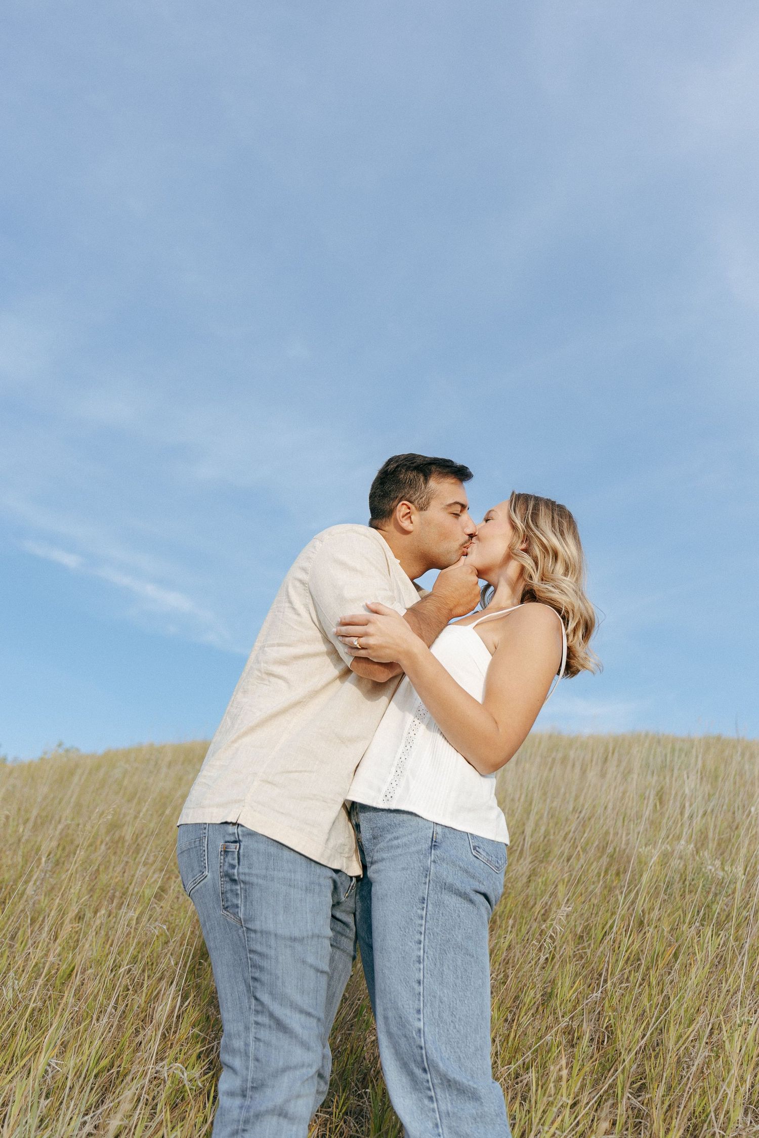 A romantic scene on a hillside with two people in jeans and white shirts against blue sky.