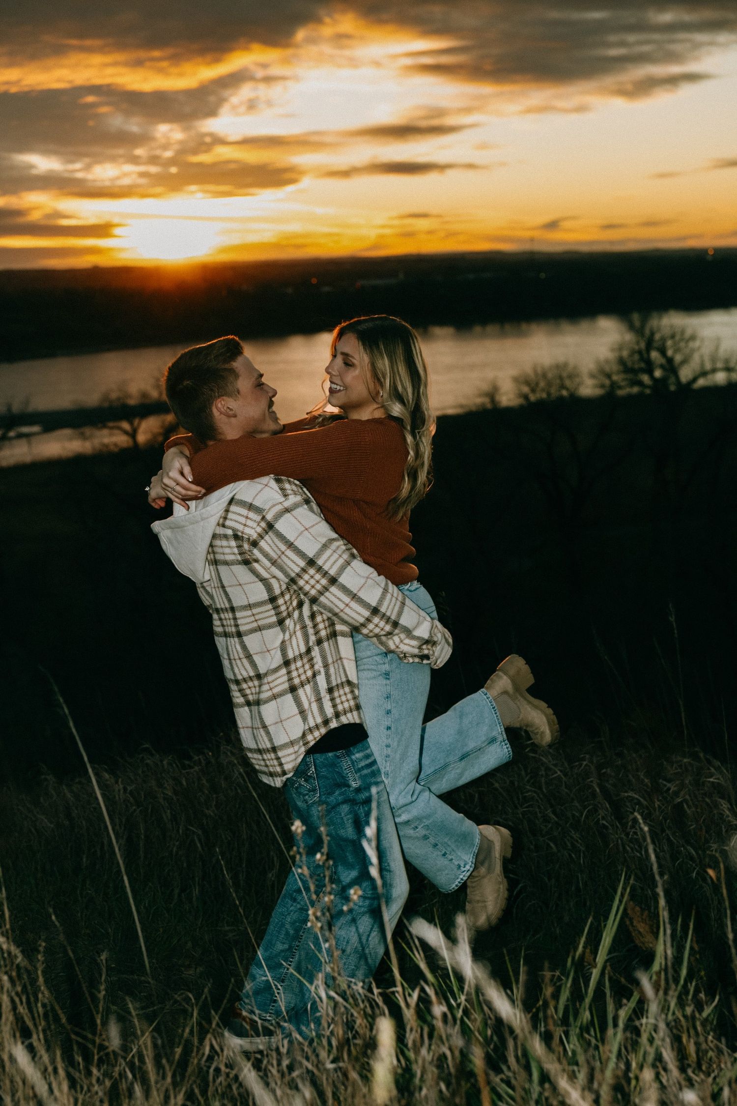 Romantic couple in rustic outfits share an intimate moment against a golden sunset backdrop.