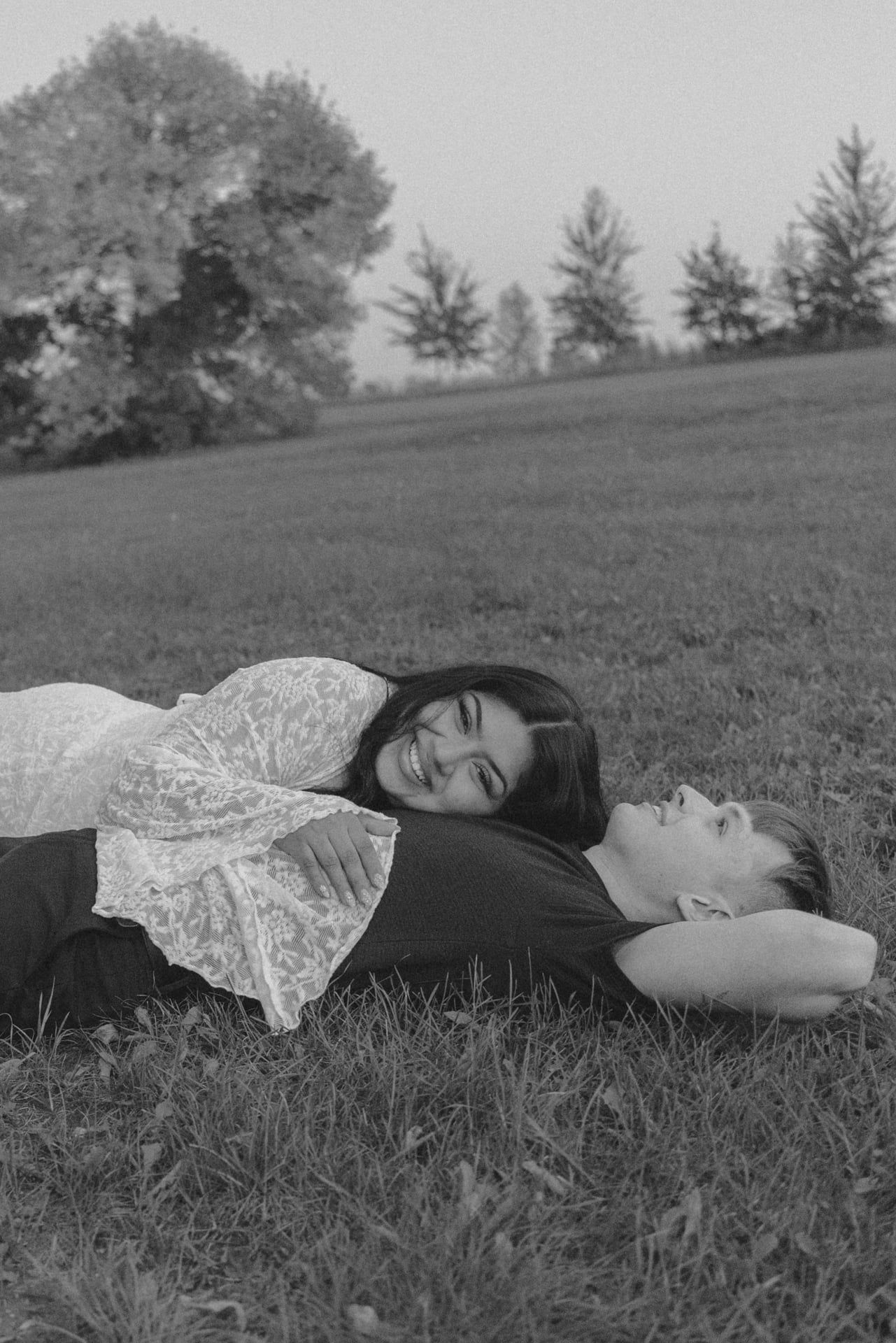 girl laying on mans chest in grassy field laughing and looking at camera