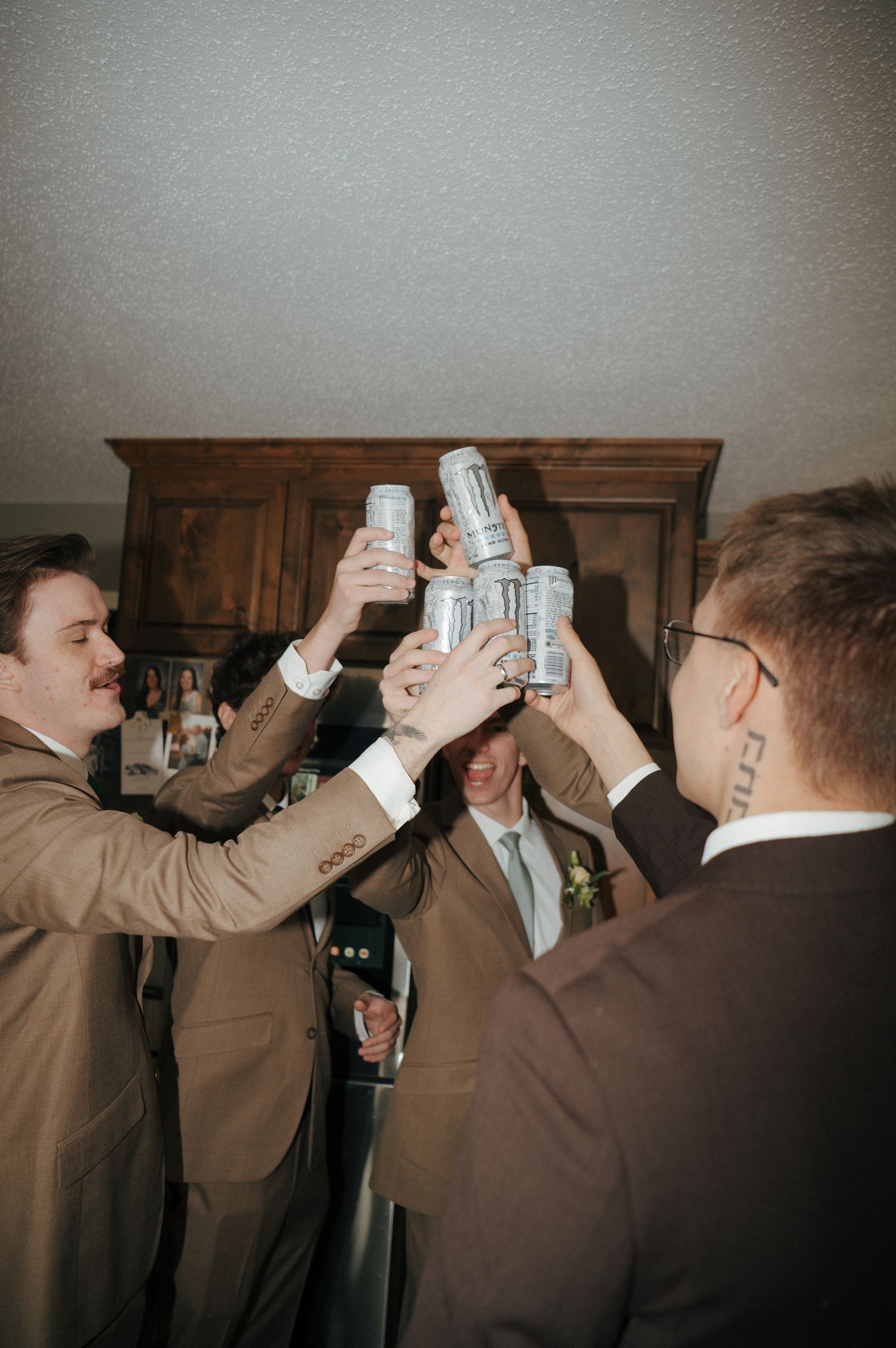 Groomsmen in brown suits toasting with beer cans before a wedding ceremony.