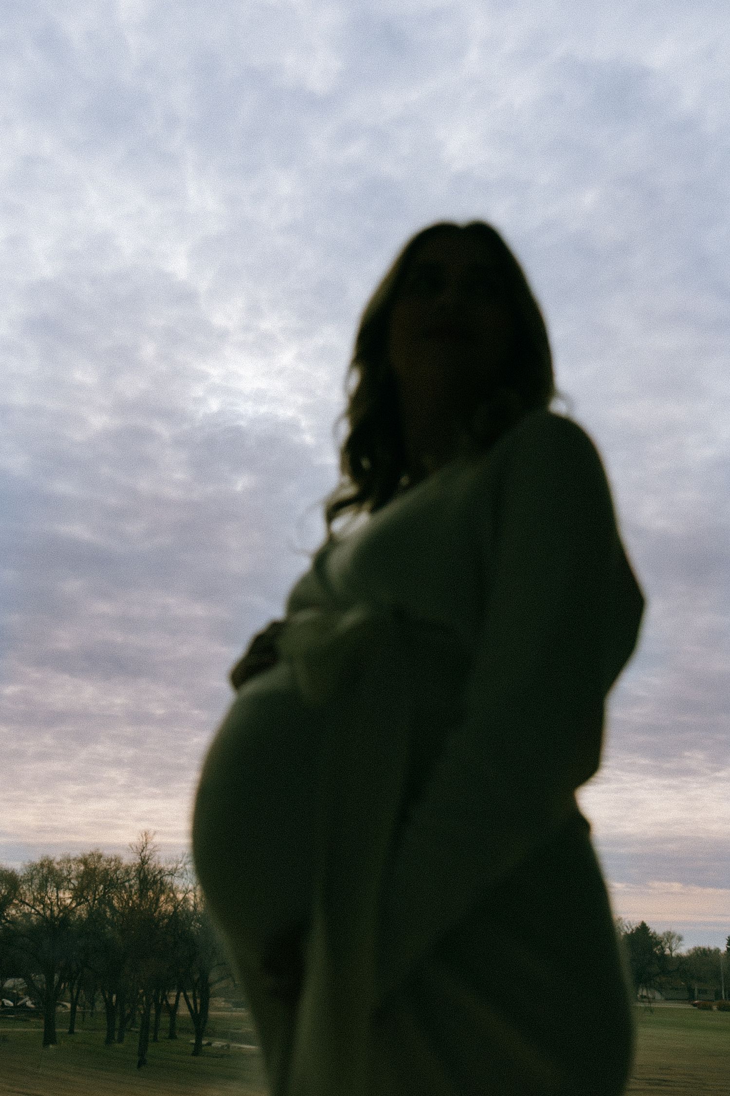 Mom holding baby bump with sunset behind her in Heritage Center