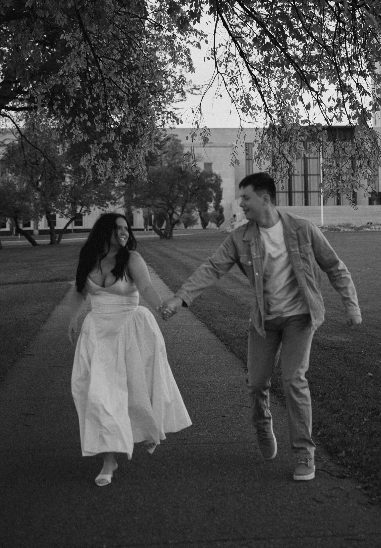 couple running holding hands laughing for engagement session on Bismarck Capitol grounds