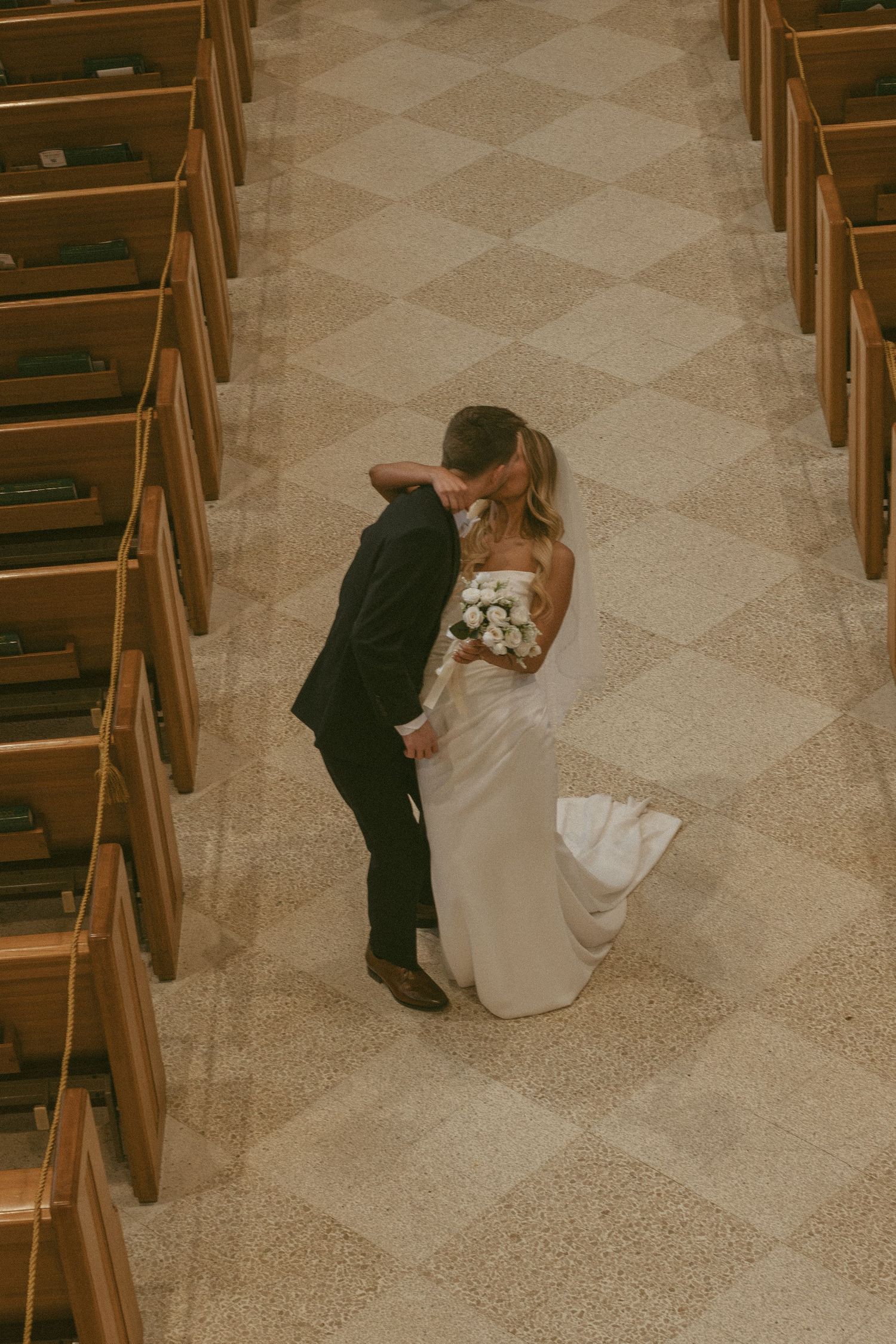Overhead view of a couple sharing an intimate moment in a church with wooden pews.