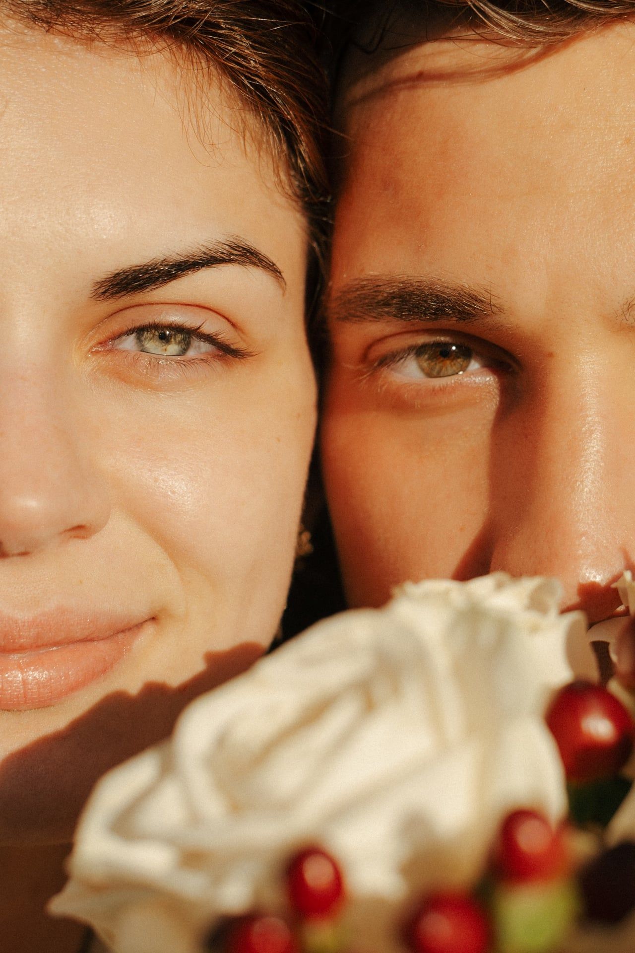 Close up portrait of two people with whipped cream and berries in warm sunlit setting.