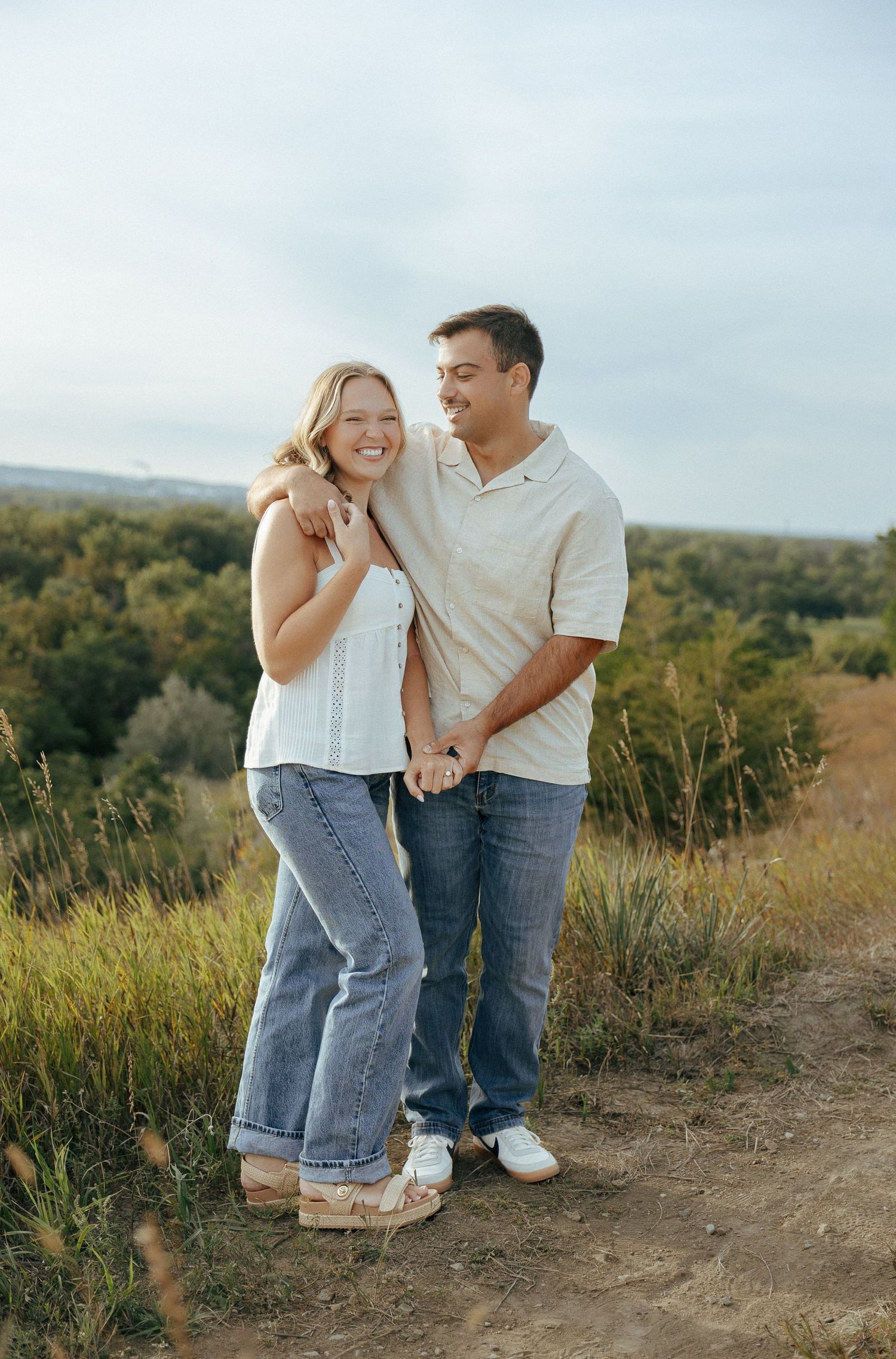A couple shares an intimate moment together on a hilltop trail during golden hour.