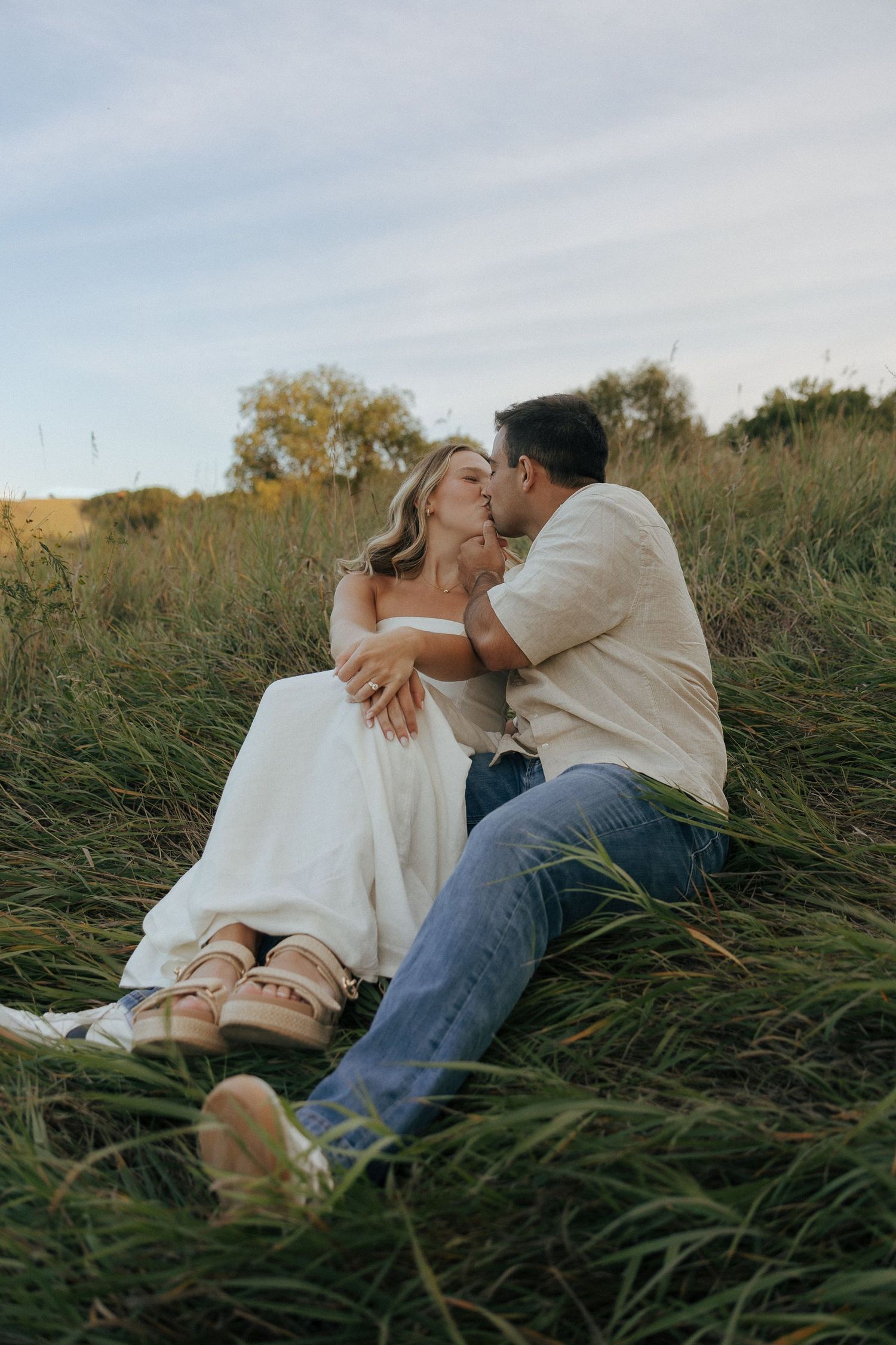 A couple shares an intimate moment while resting in a field of tall grass at sunset.