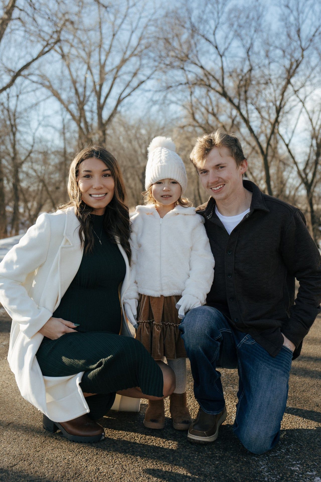 photos of mom and dad crouching down next to daughter in snowy trees in Bismarck