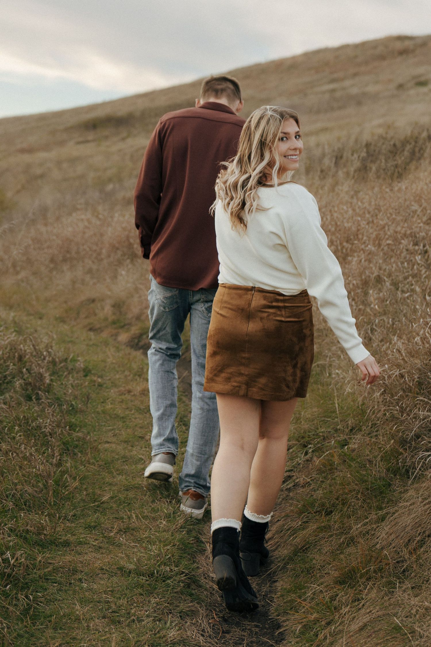 Two people walking along a grassy hillside path during golden hour.