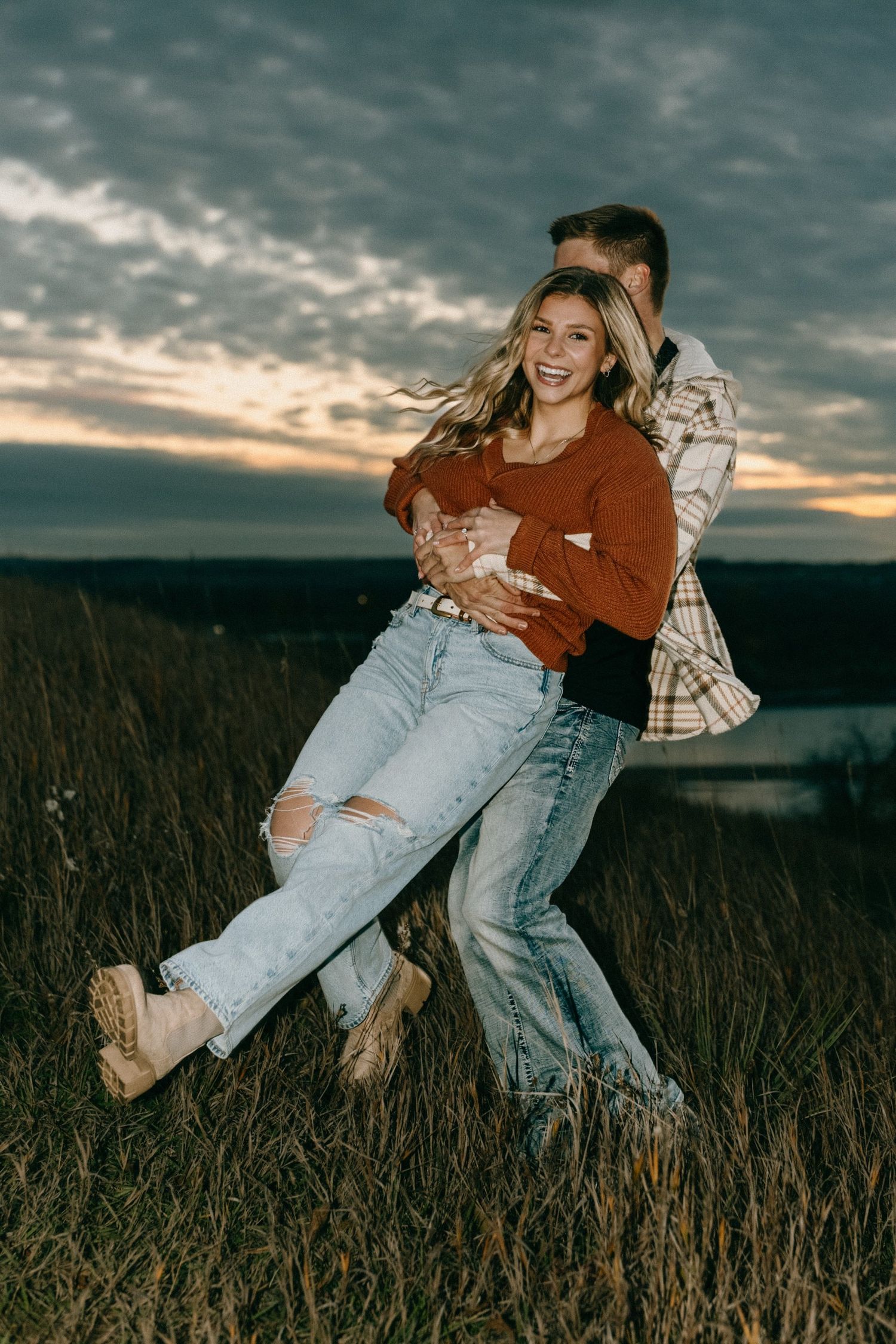 Joyful couple sharing laughs and embraces in field during golden hour.