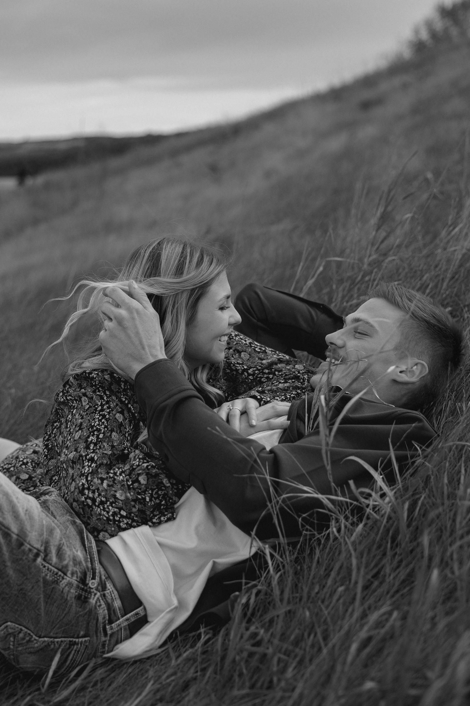 Intimate black and white portrait of couple lying in meadow grass.
