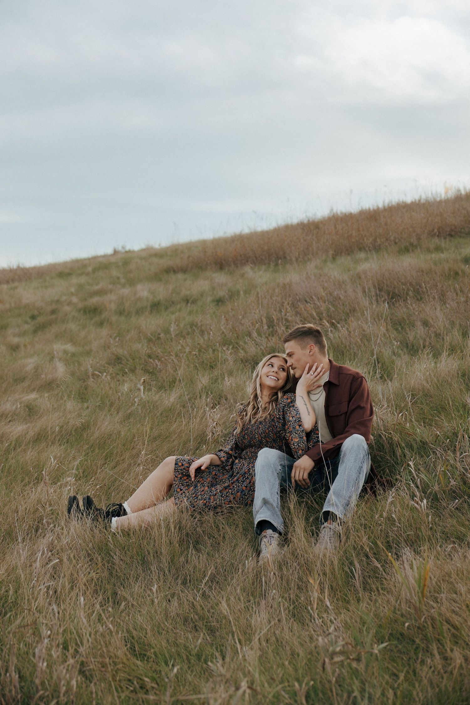 Couple sharing tender moment while relaxing in tall grass on hillside.