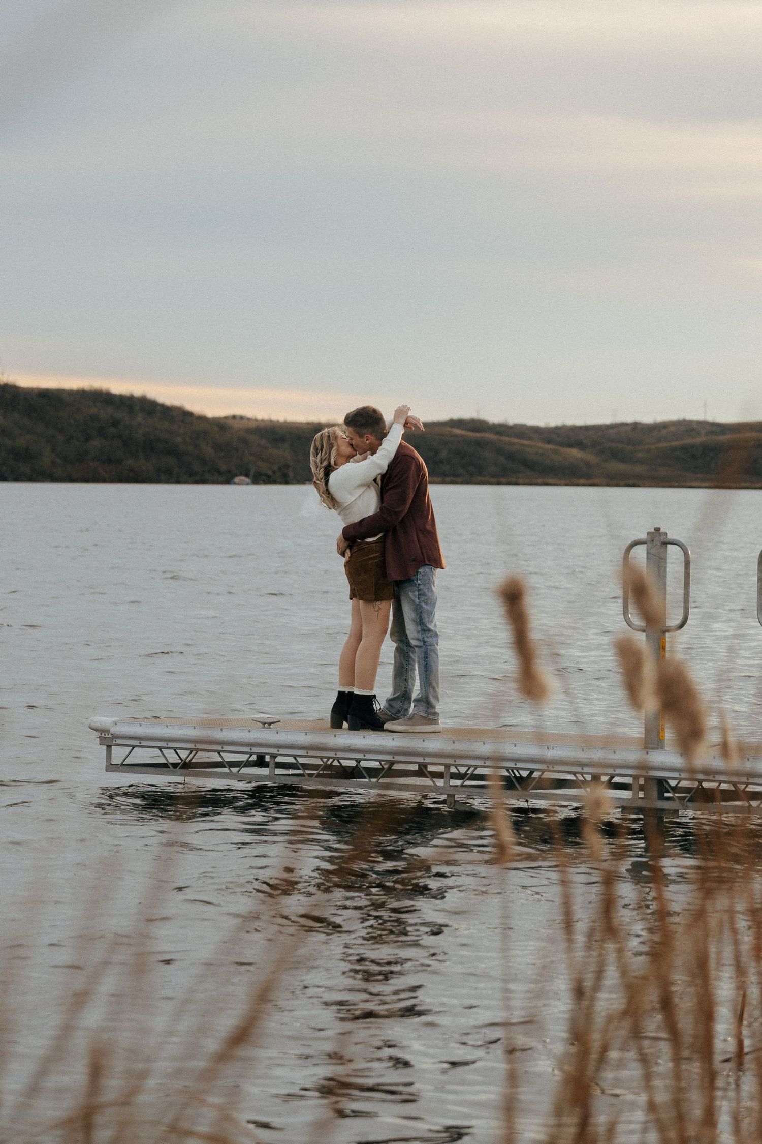Two people share a tender moment on a lakeside dock during golden hour.